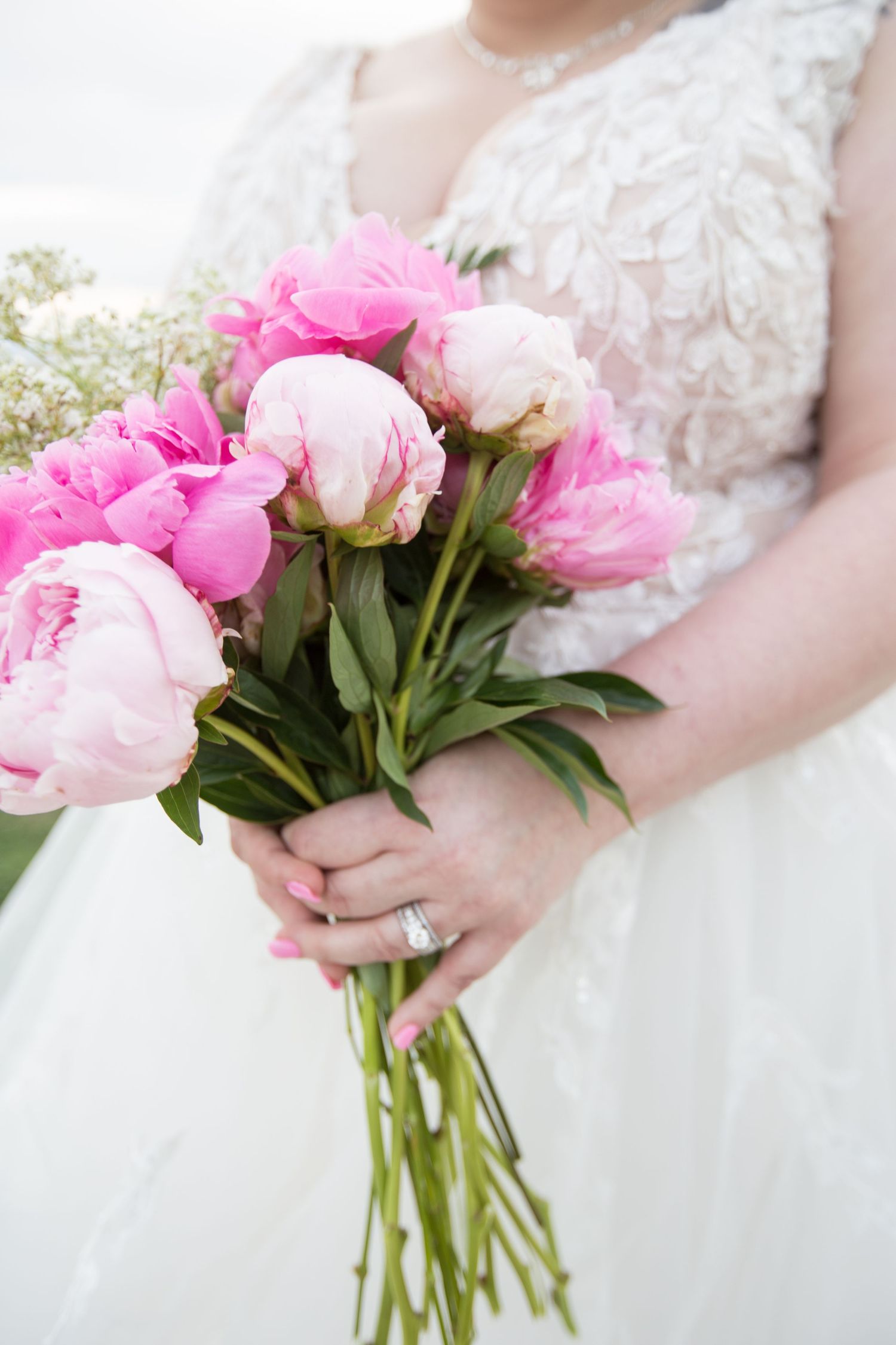 Close-up detail of pink peonies bouquet against white wedding dress lace.