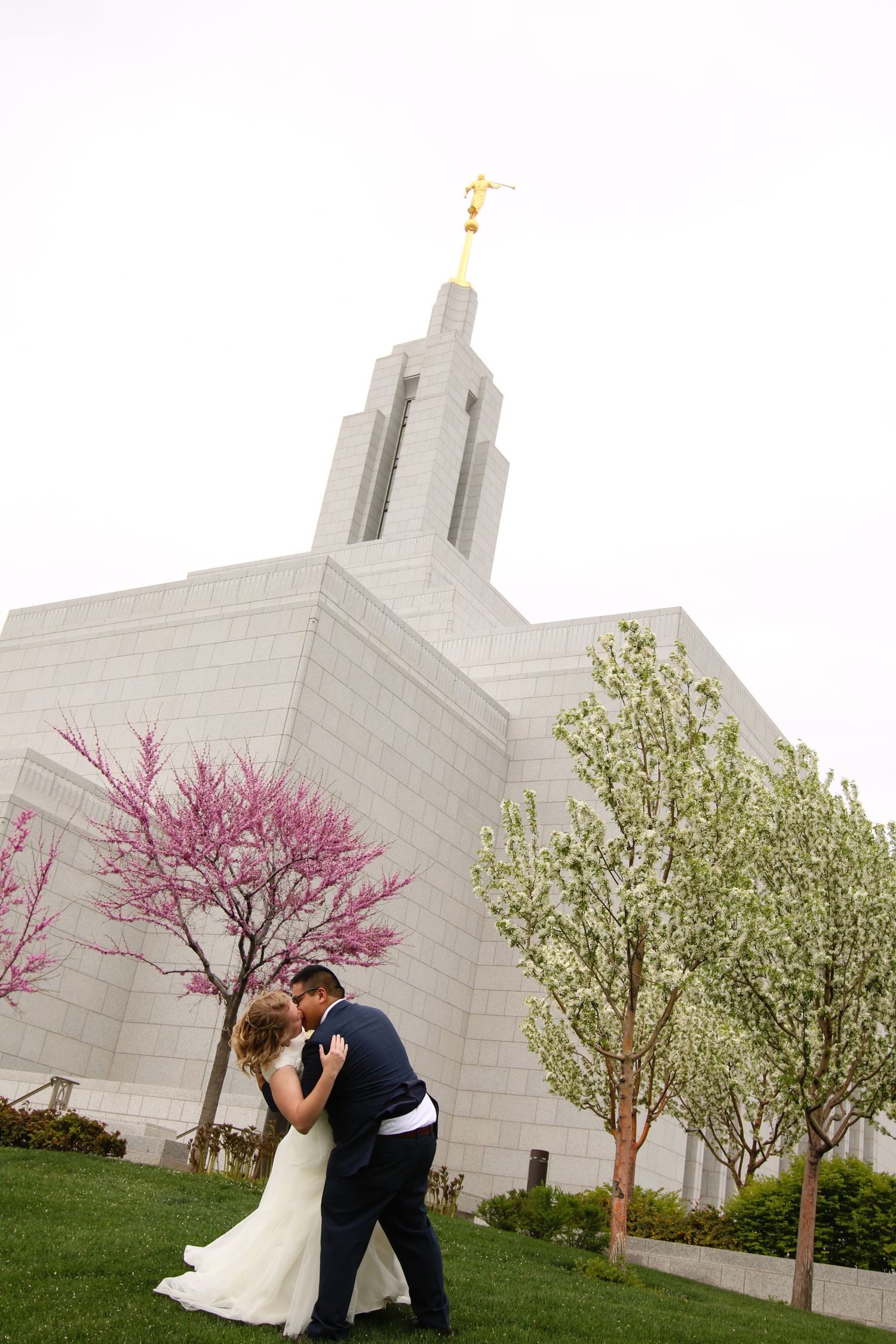 Newlyweds sharing romantic moments in front of a white temple with blooming spring trees.