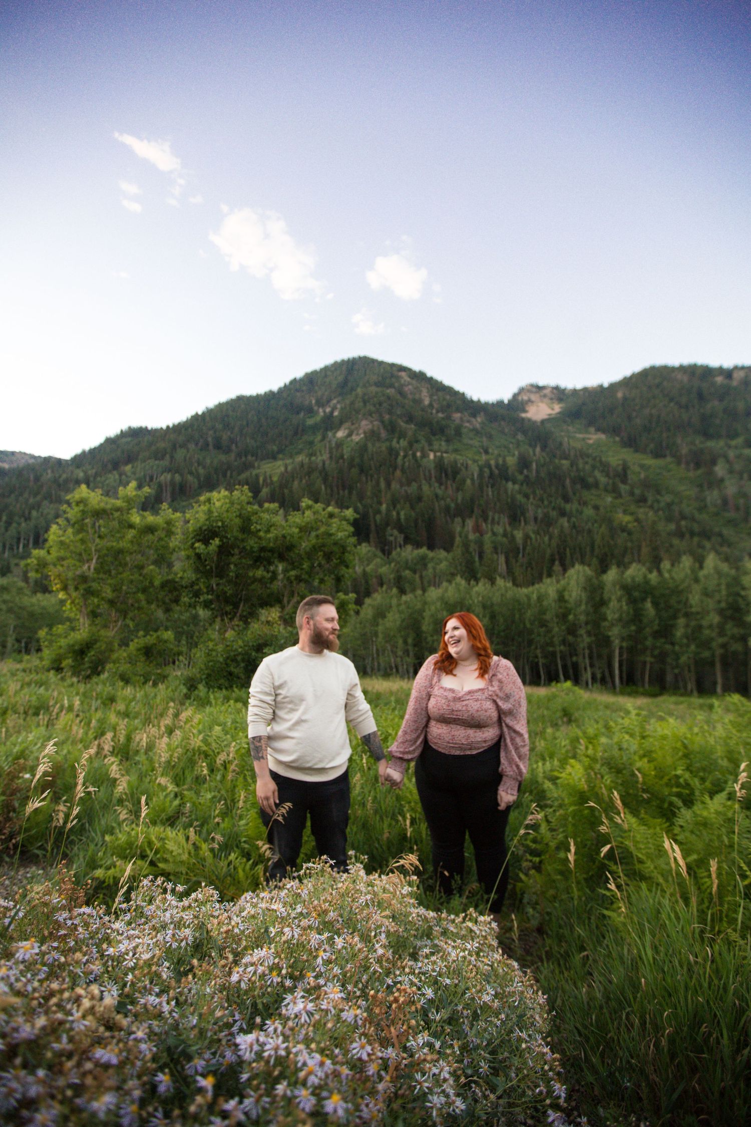 A couple walks through a wildflower meadow with mountain views.
