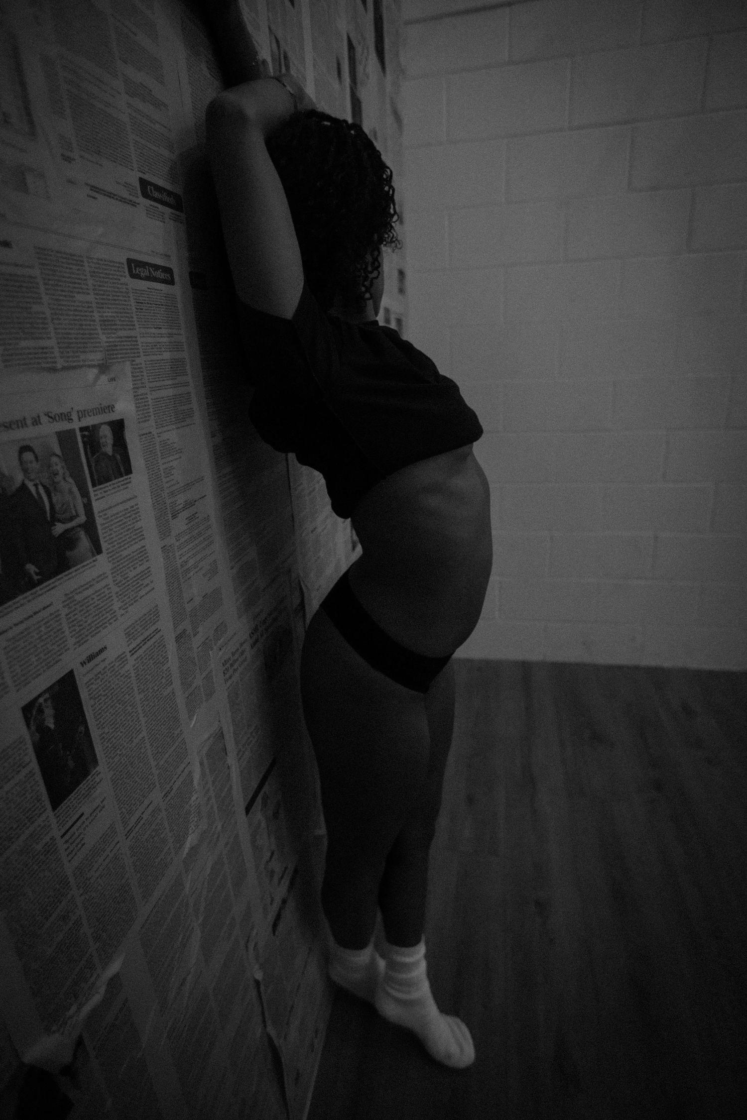 Dark artistic portrait against wall covered in papers and posters.