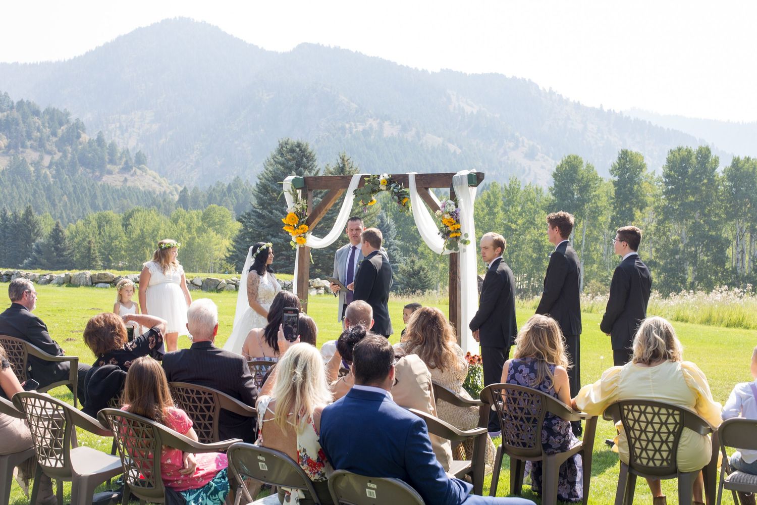 Outdoor wedding ceremony with mountain views and guests seated on white chairs.