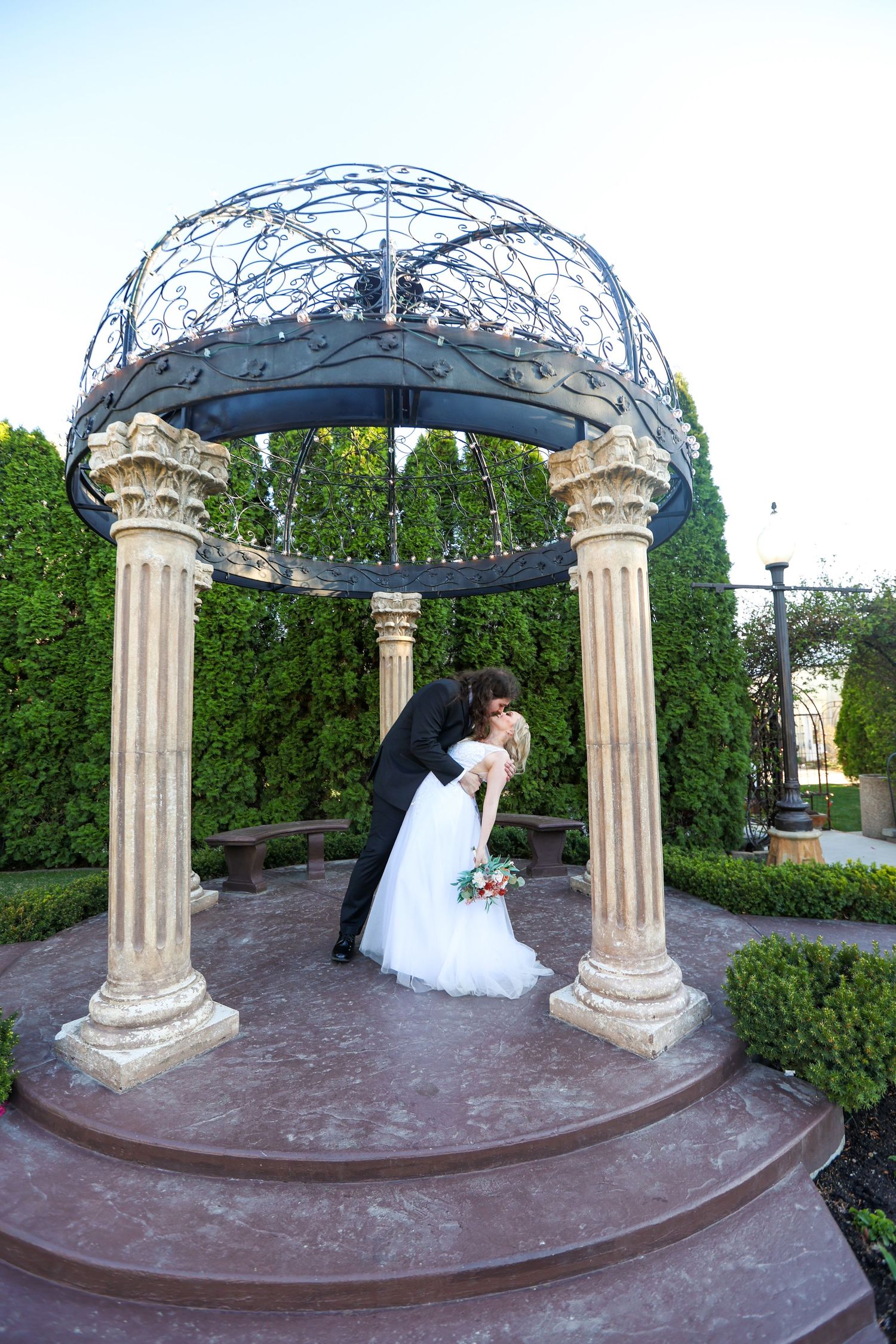 Elegant garden wedding ceremony setup with white columns and metal dome arbor.