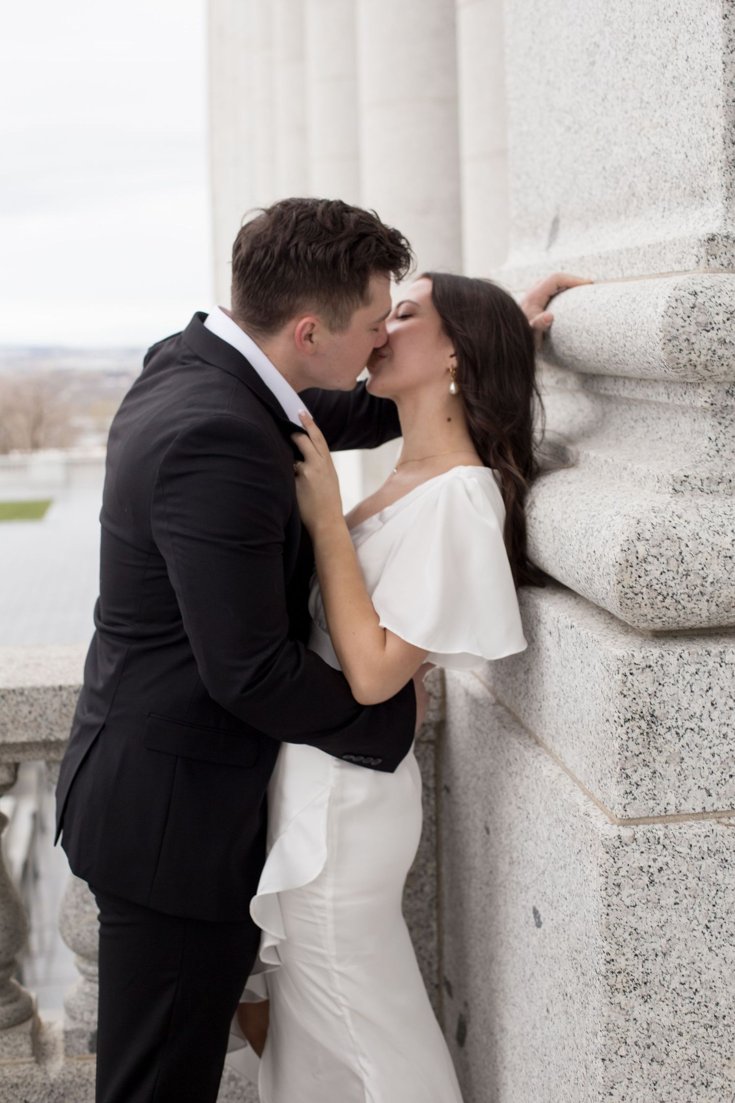 A passionate moment between newlyweds against a stone column on an elegant balcony.