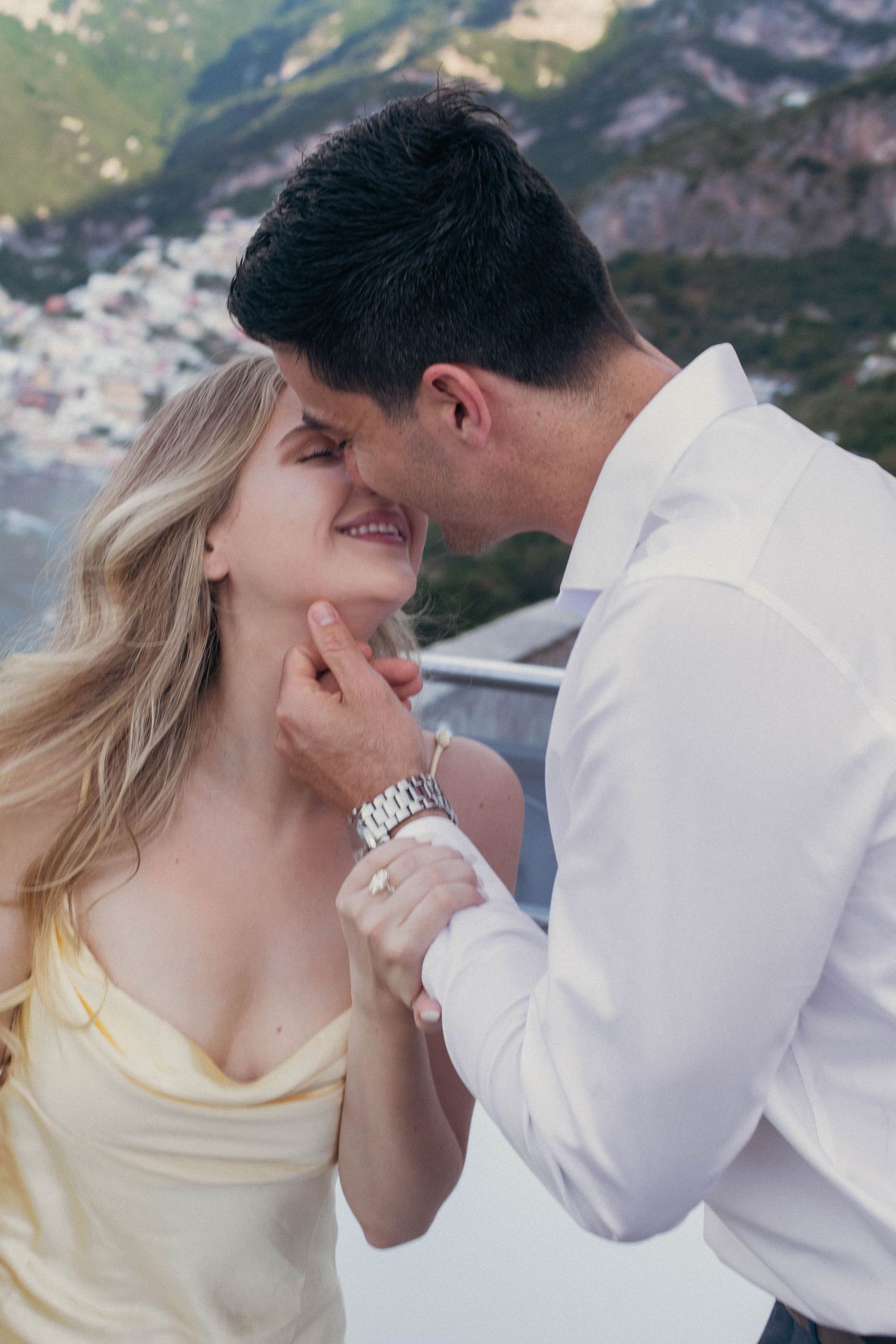 Romantic couple almost kissing with man gently holding womans chin against Positano hillside backdrop.