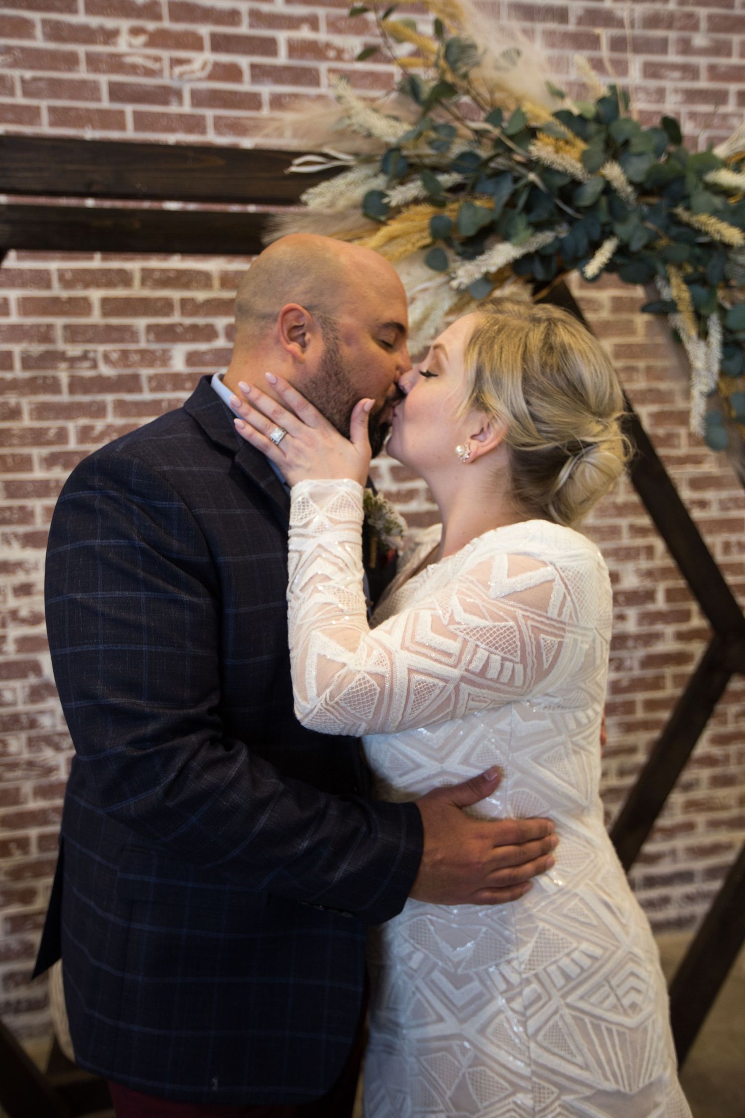 Bride and groom share a first kiss at their wedding altar decorated with greenery and a wooden arch.