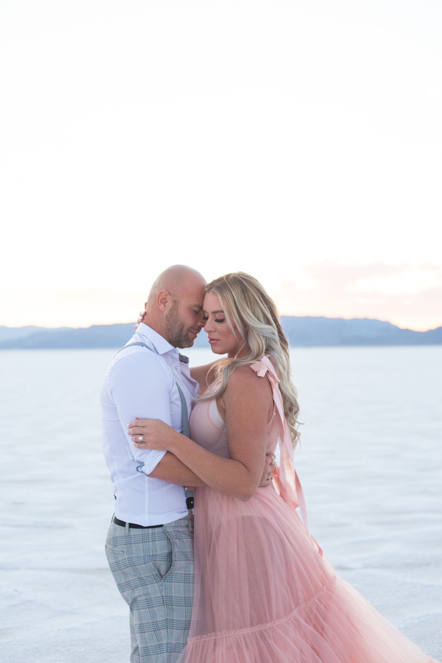 Romantic beach photoshoot features couple in pink dress and formal wear.