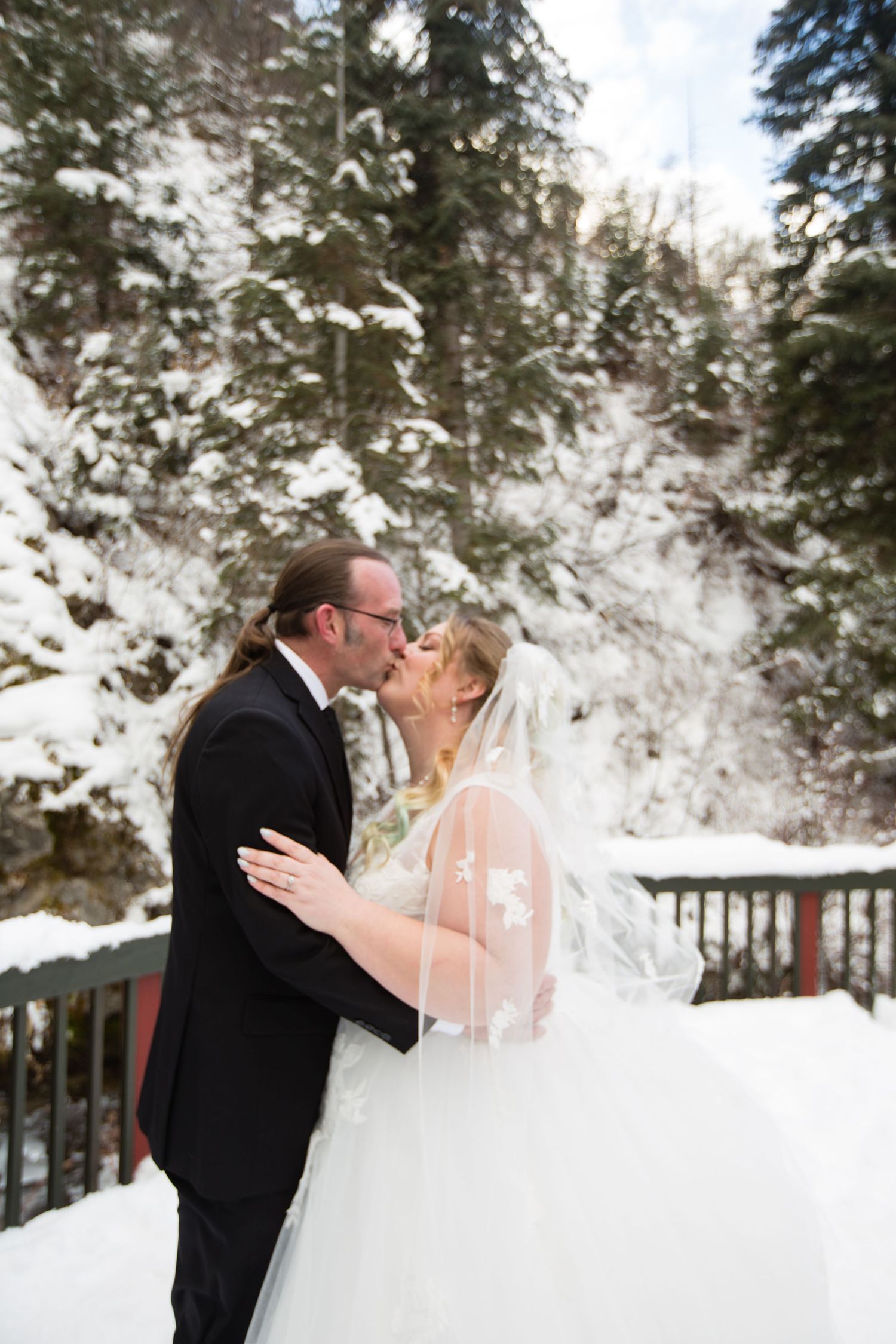 Romantic winter wedding portrait with couple embracing against snowy mountain backdrop.