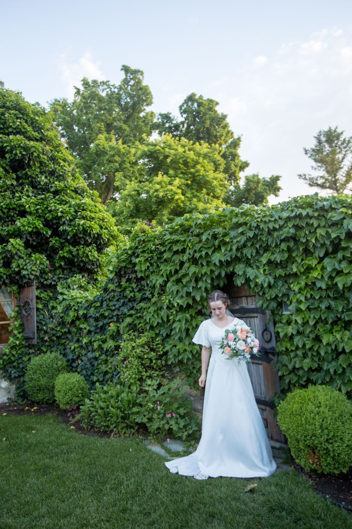 White gown flowing in a lush garden setting with ivy-covered walls.