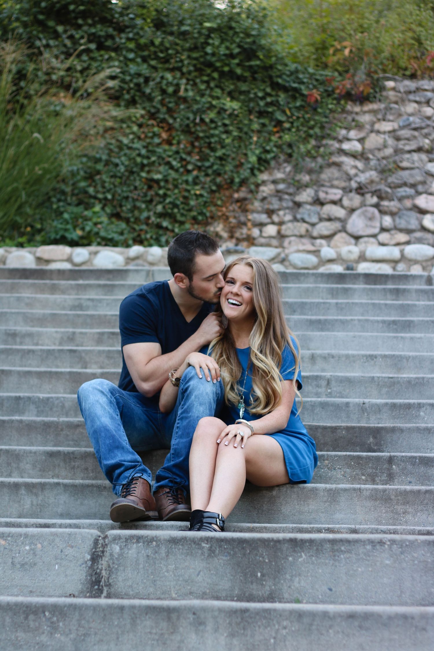 A couple shares a playful moment while sitting on concrete steps outdoors.