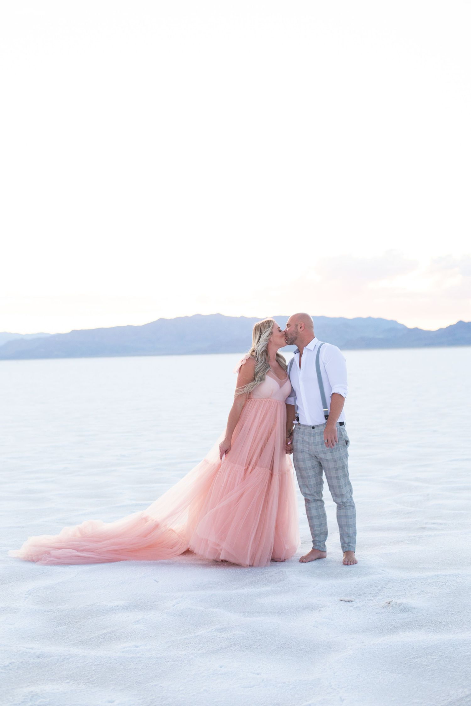 Romantic sunset portraits on salt flats with mountains and pink tulle dress.