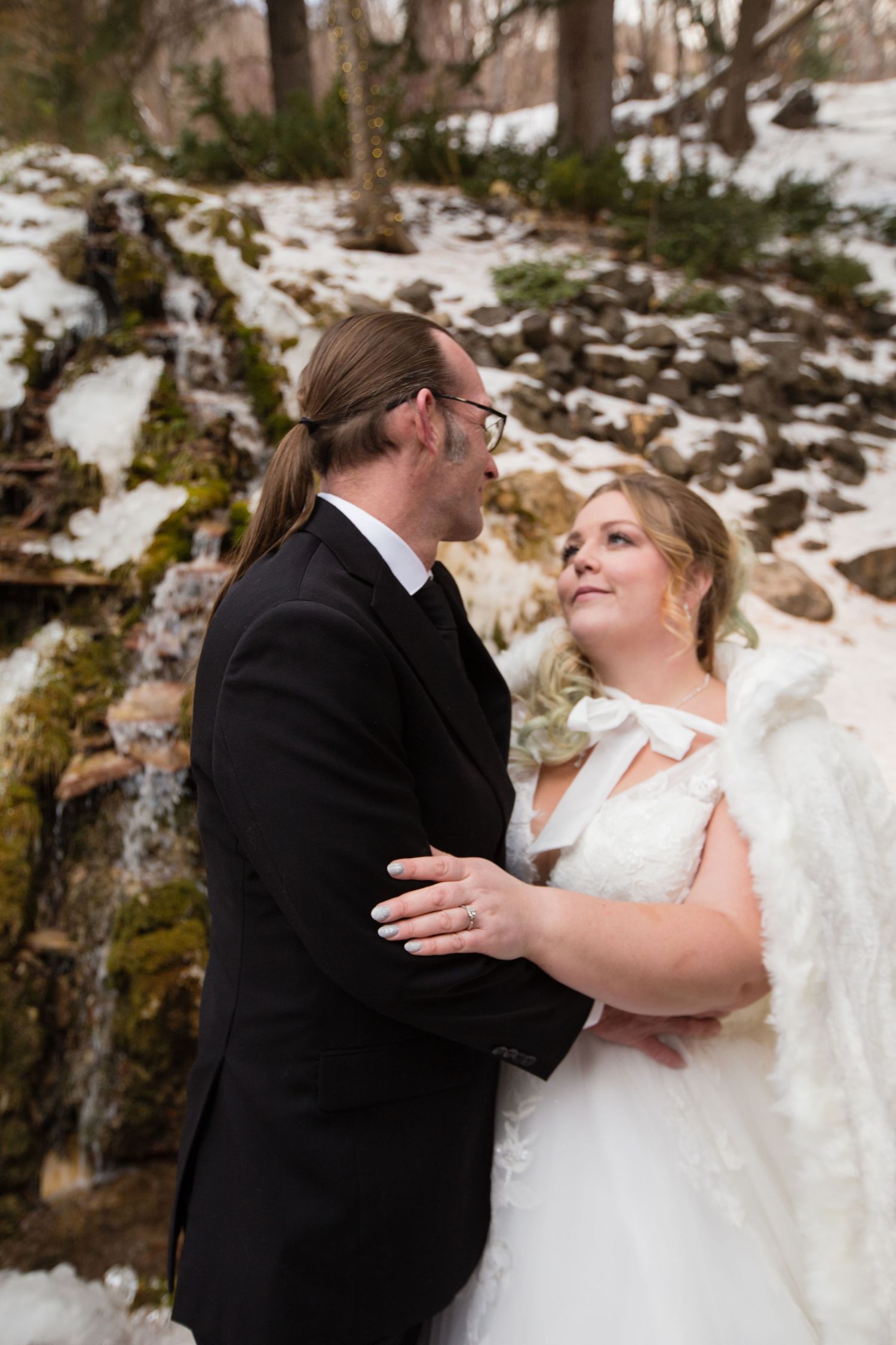 Candid wedding photography showing tender moments between newlyweds in snowy outdoor setting.