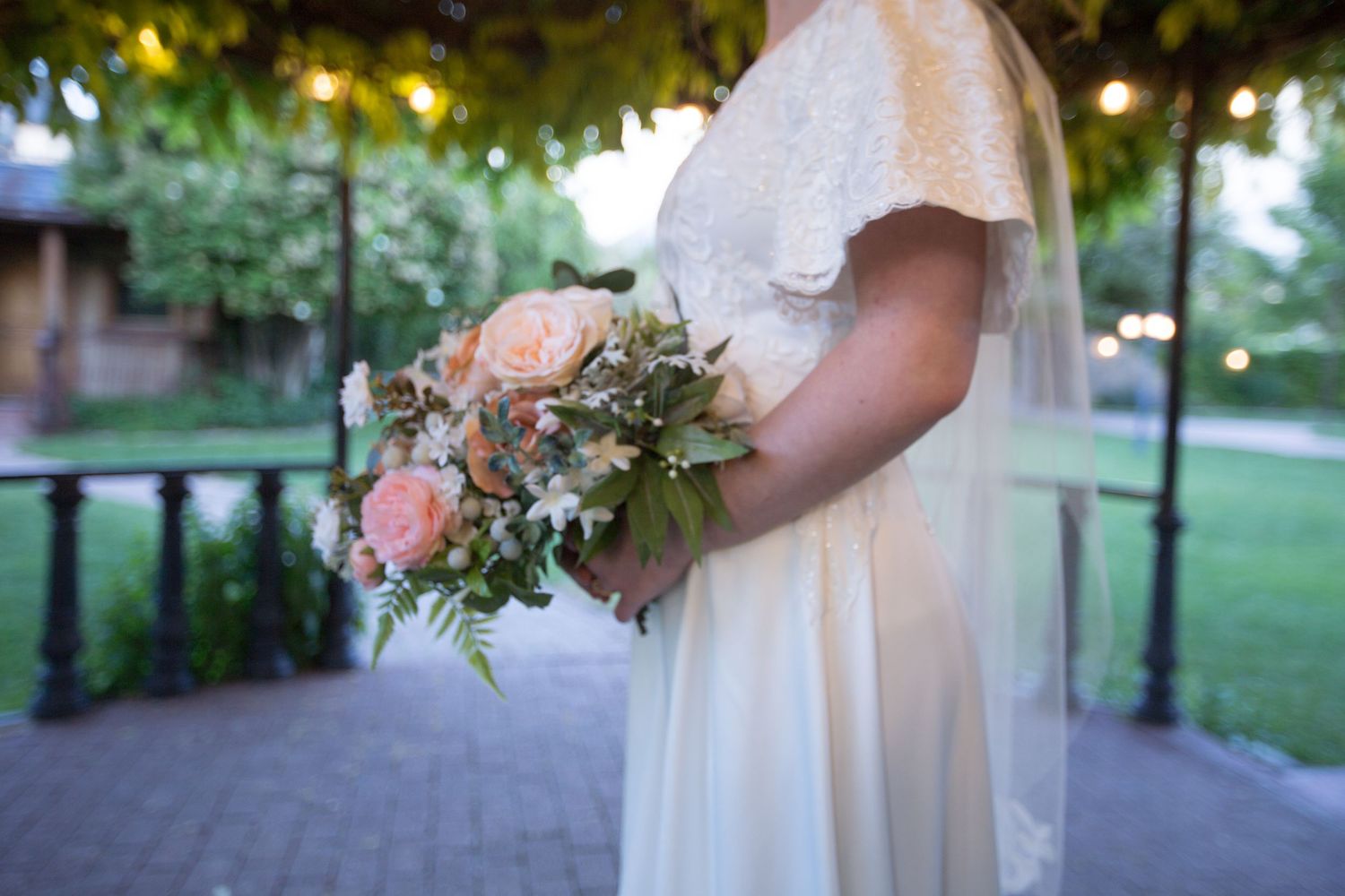 A bridal bouquet with pink and white flowers held against a white wedding dress.