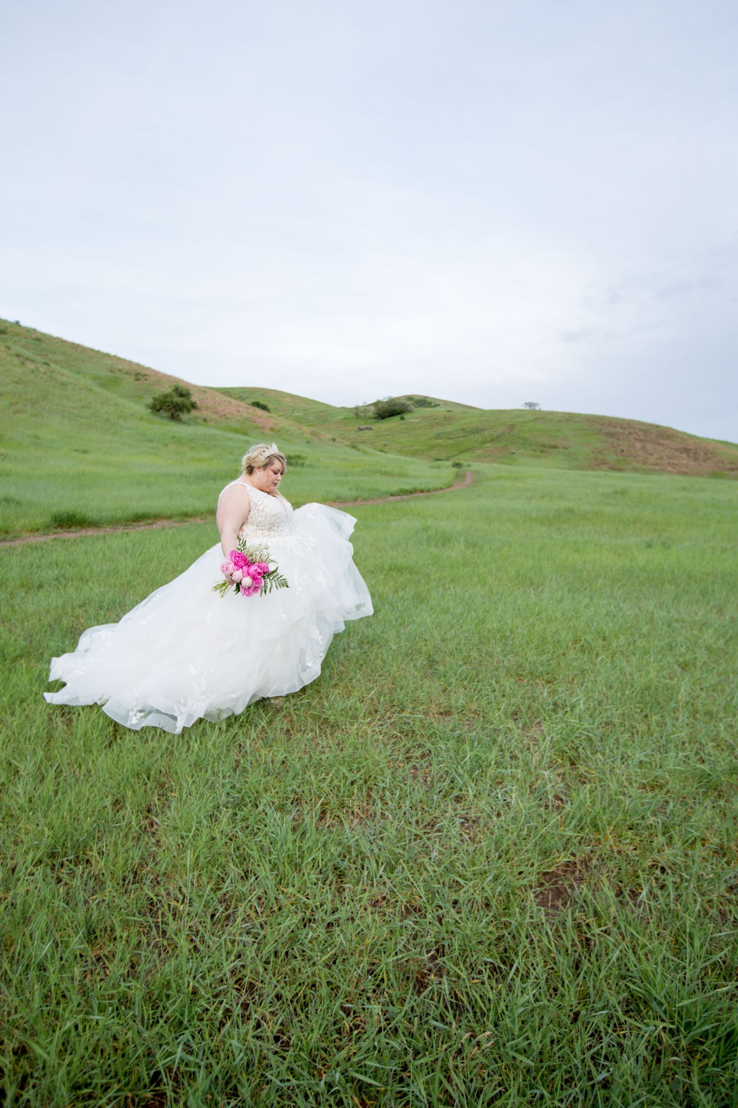 Flowing white bridal gown spreads across lush green grass in a scenic outdoor setting.