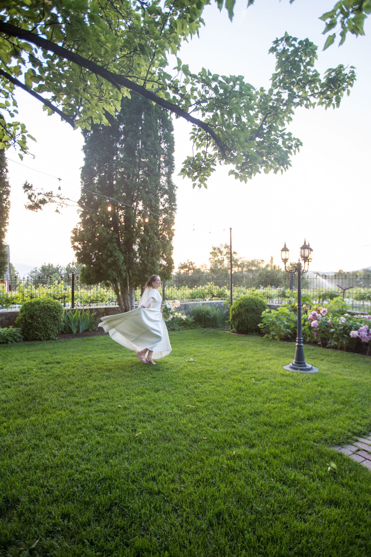 A flowing white dress twirls on a lush green lawn at sunset.