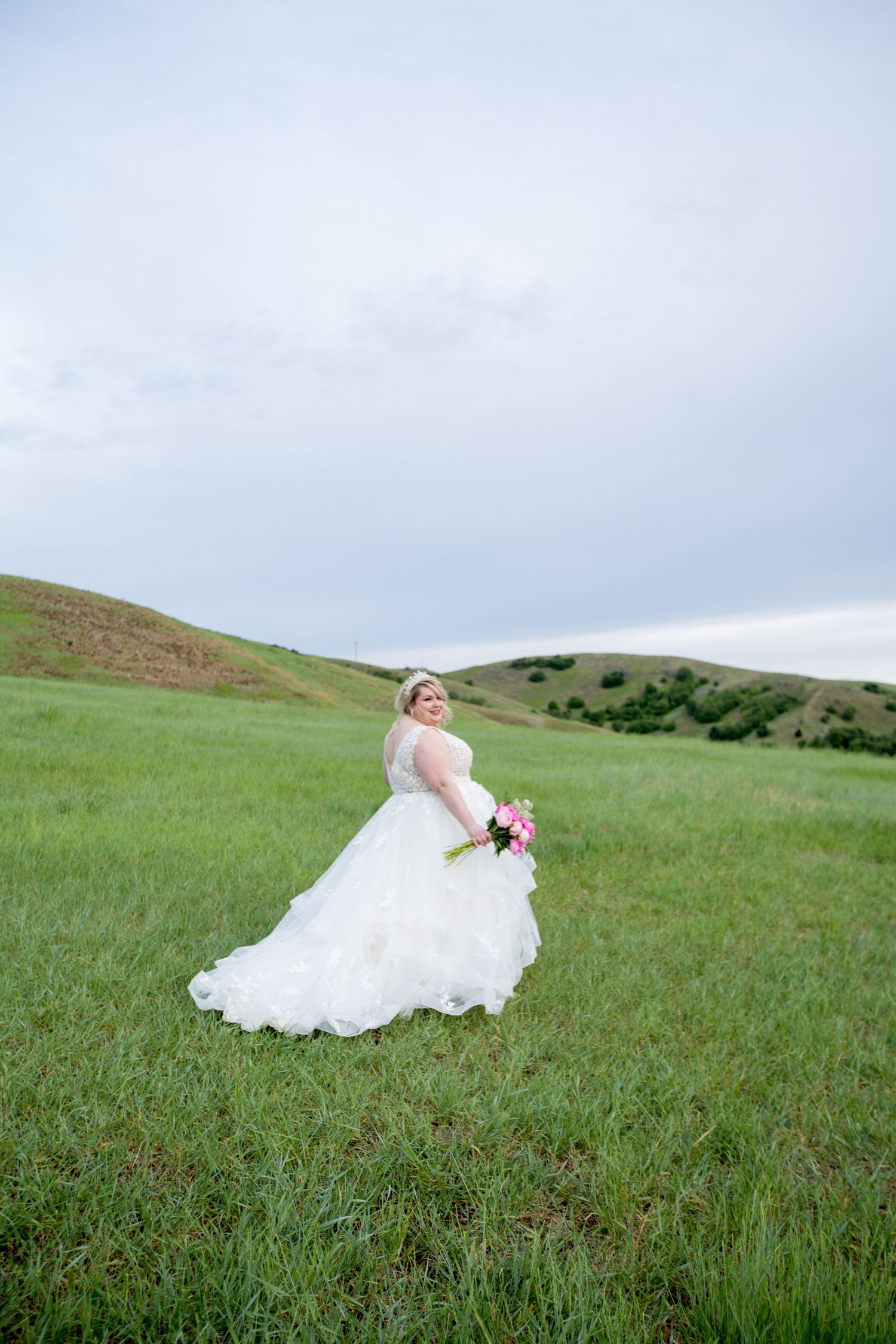 Wedding dress billows in the wind on a grassy hillside landscape.