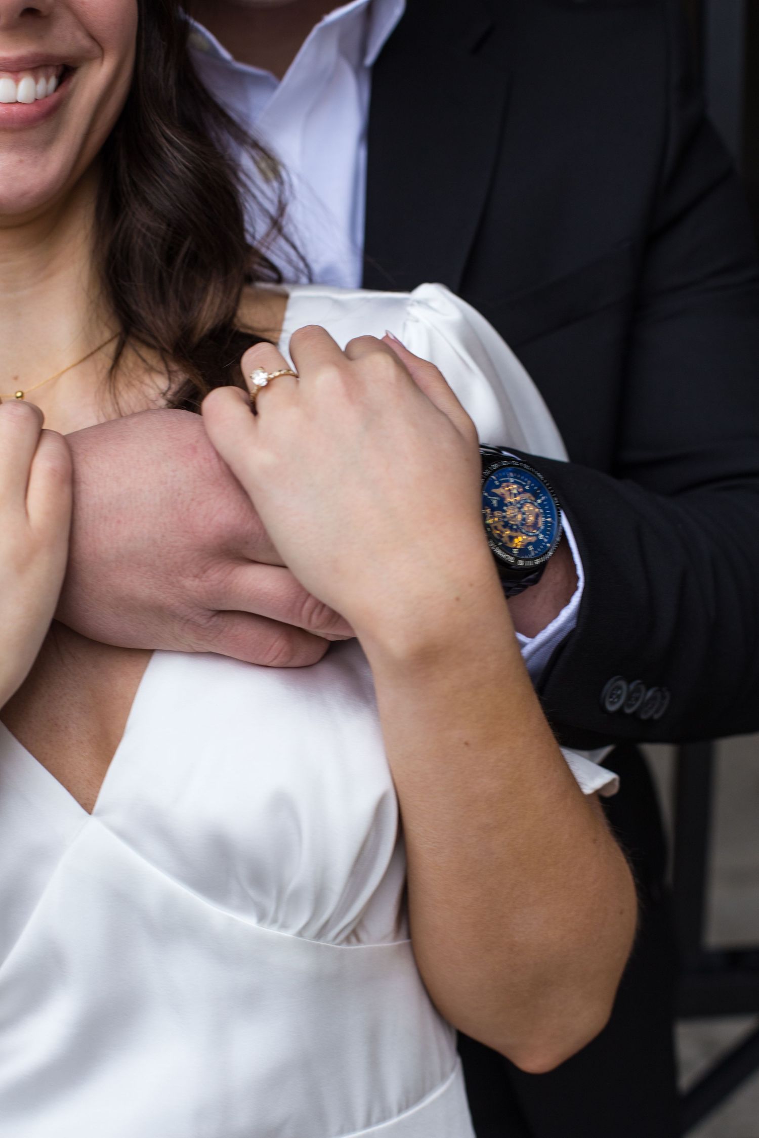 Close-up shot of hands showing off an engagement ring and blue watch against white formal attire.