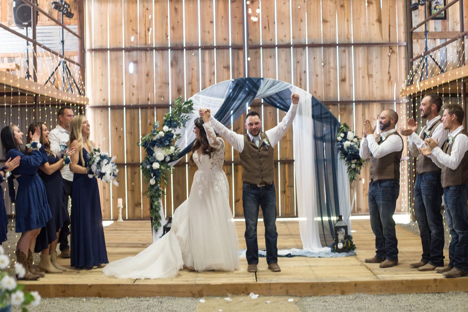 Wedding celebration in rustic barn venue with wedding party and guests cheering.