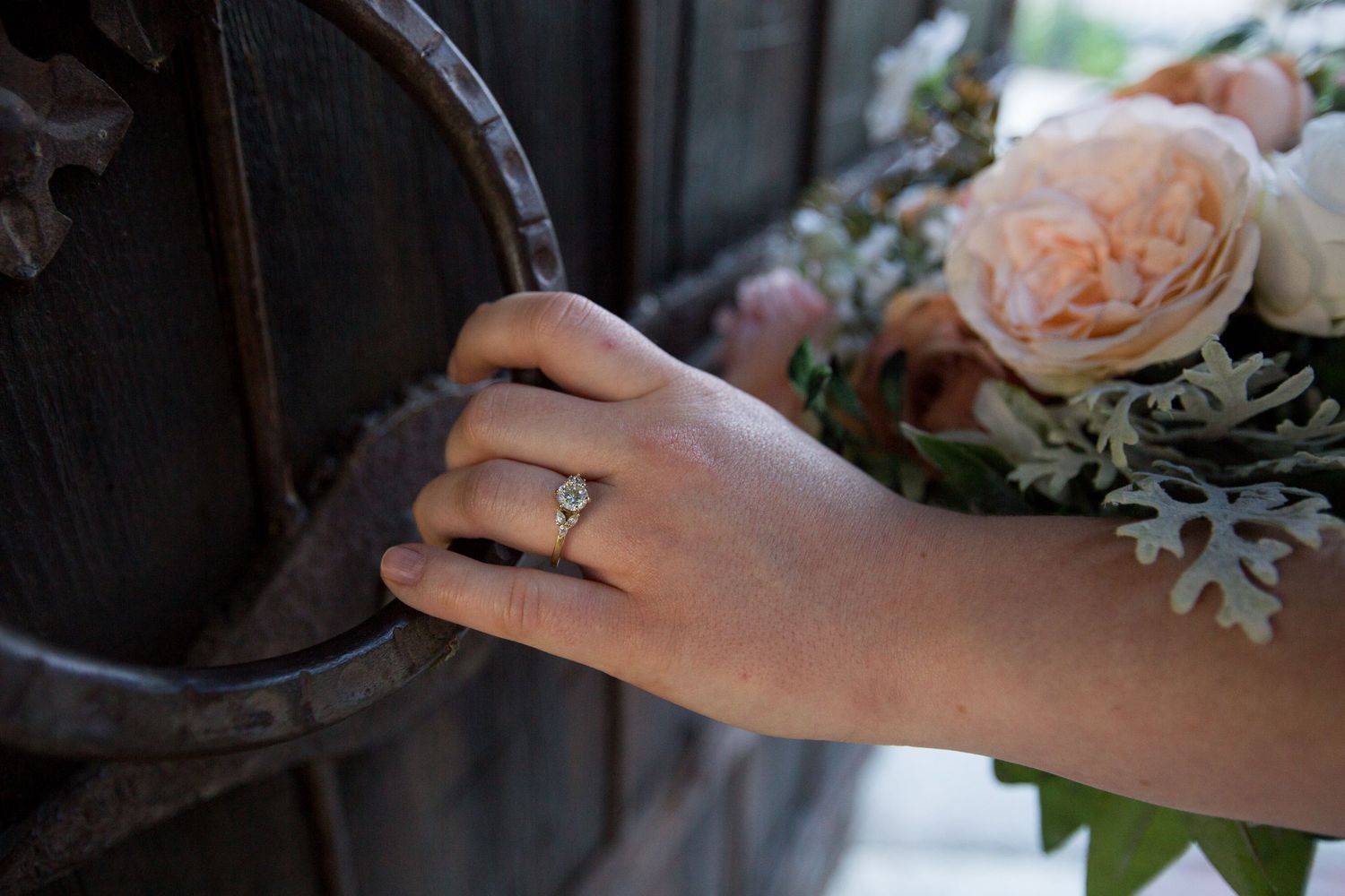 Detail shot of hands holding a romantic bouquet with peach roses and silvery foliage.