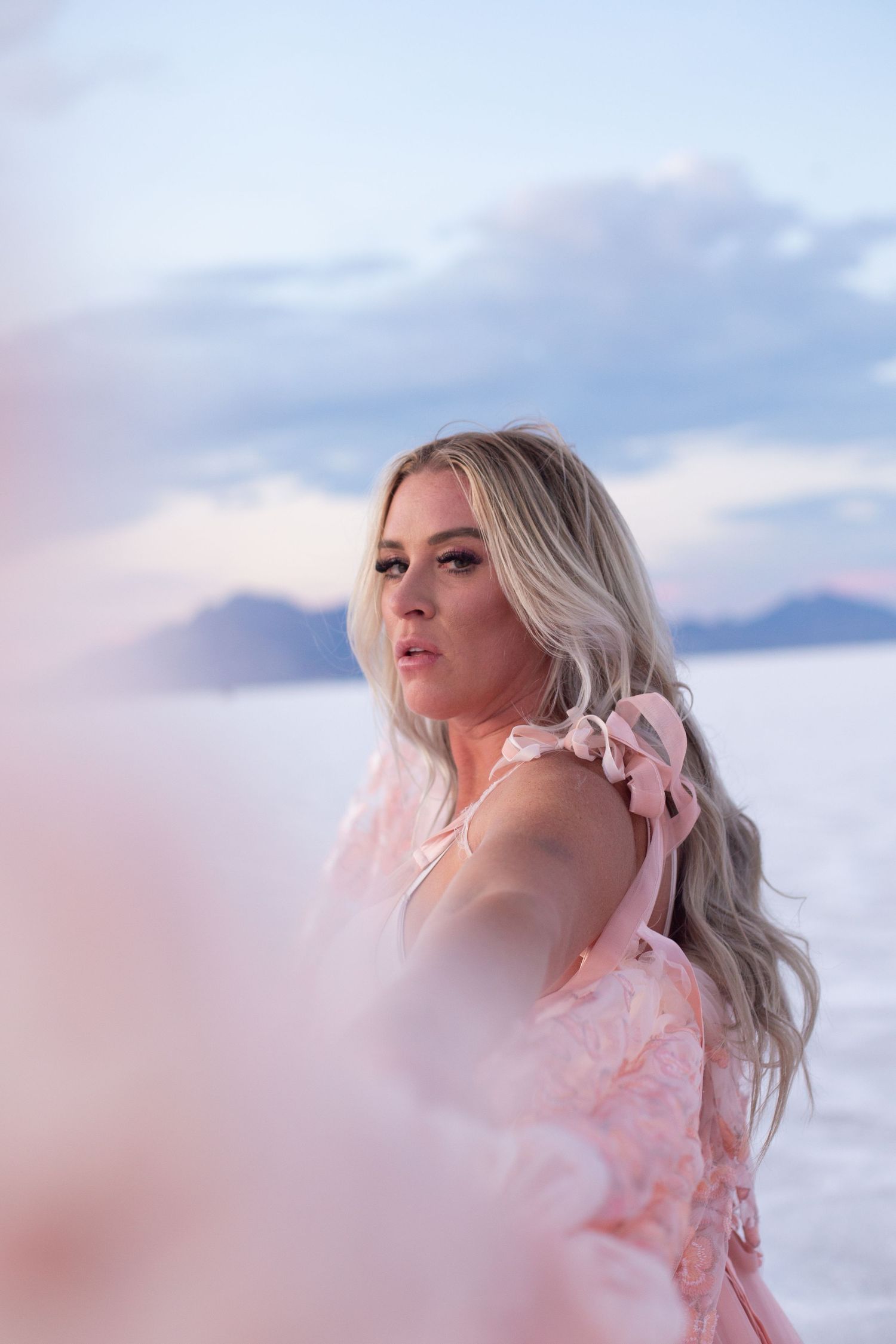 Soft pink dress details and delicate lace create a dreamy portrait against a pastel sky.