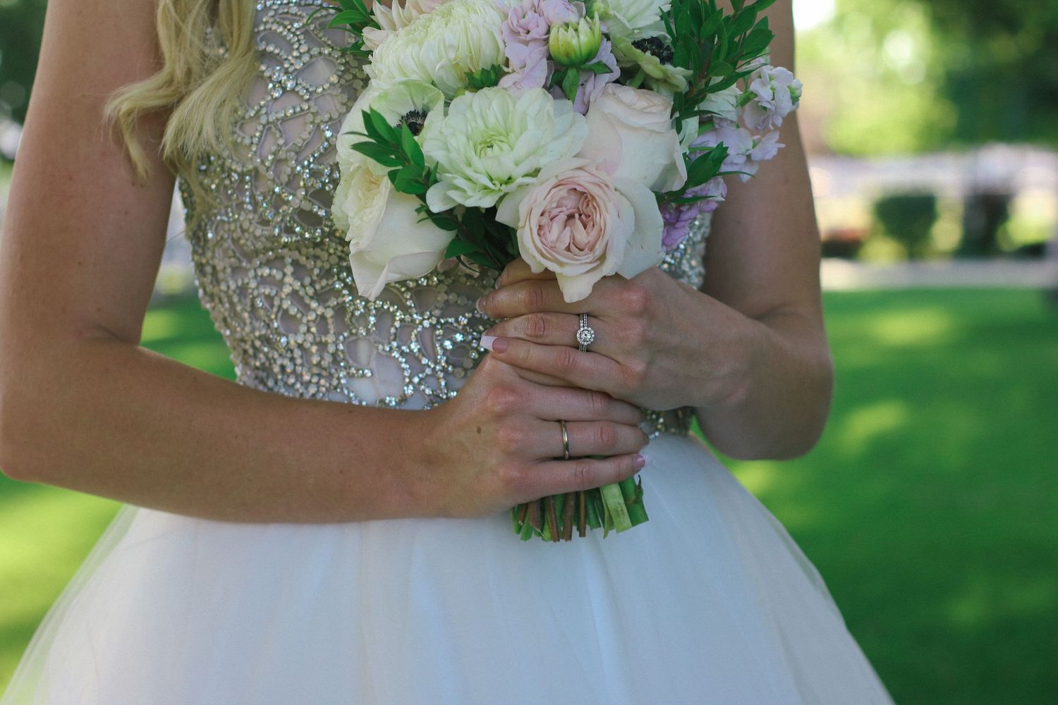 Close-up of a bridal bouquet with white and pink roses held by hands in a sparkly dress.