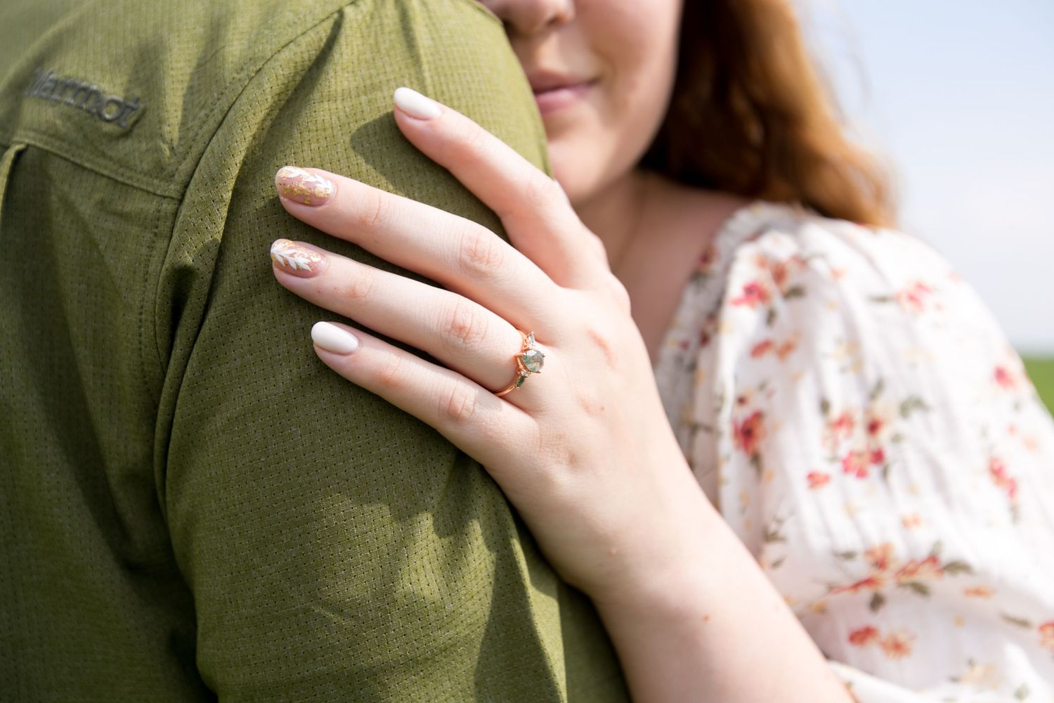 Close-up of hands with engagement ring against olive green clothing.