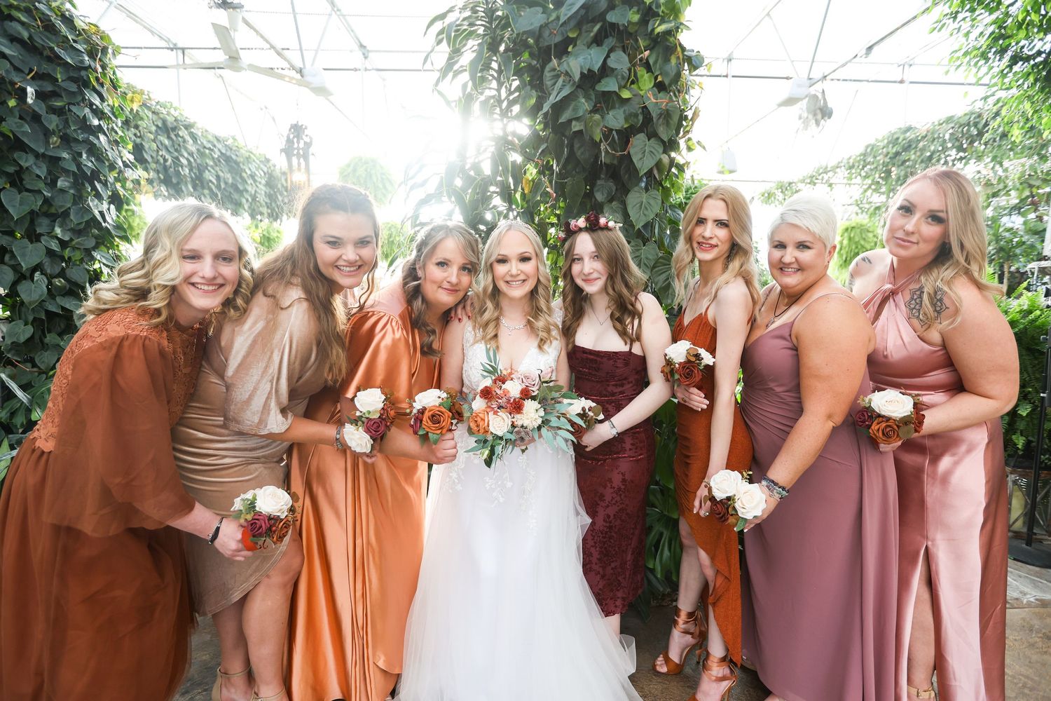 Bridesmaids in coordinating pink and rust-colored dresses pose together outdoors.