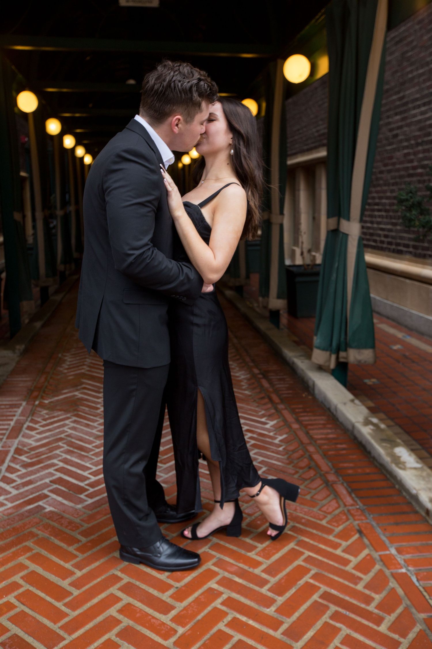 Couple sharing an intimate moment in a dimly lit brick corridor with string lights.