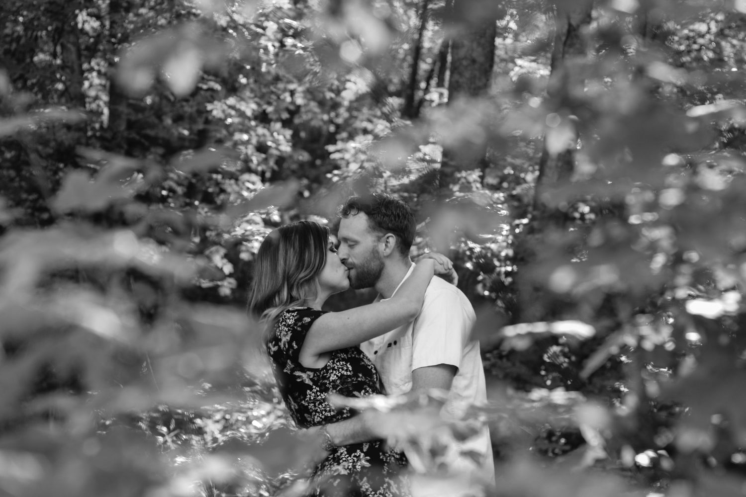 An intimate black and white portrait through soft-focus foliage and branches.