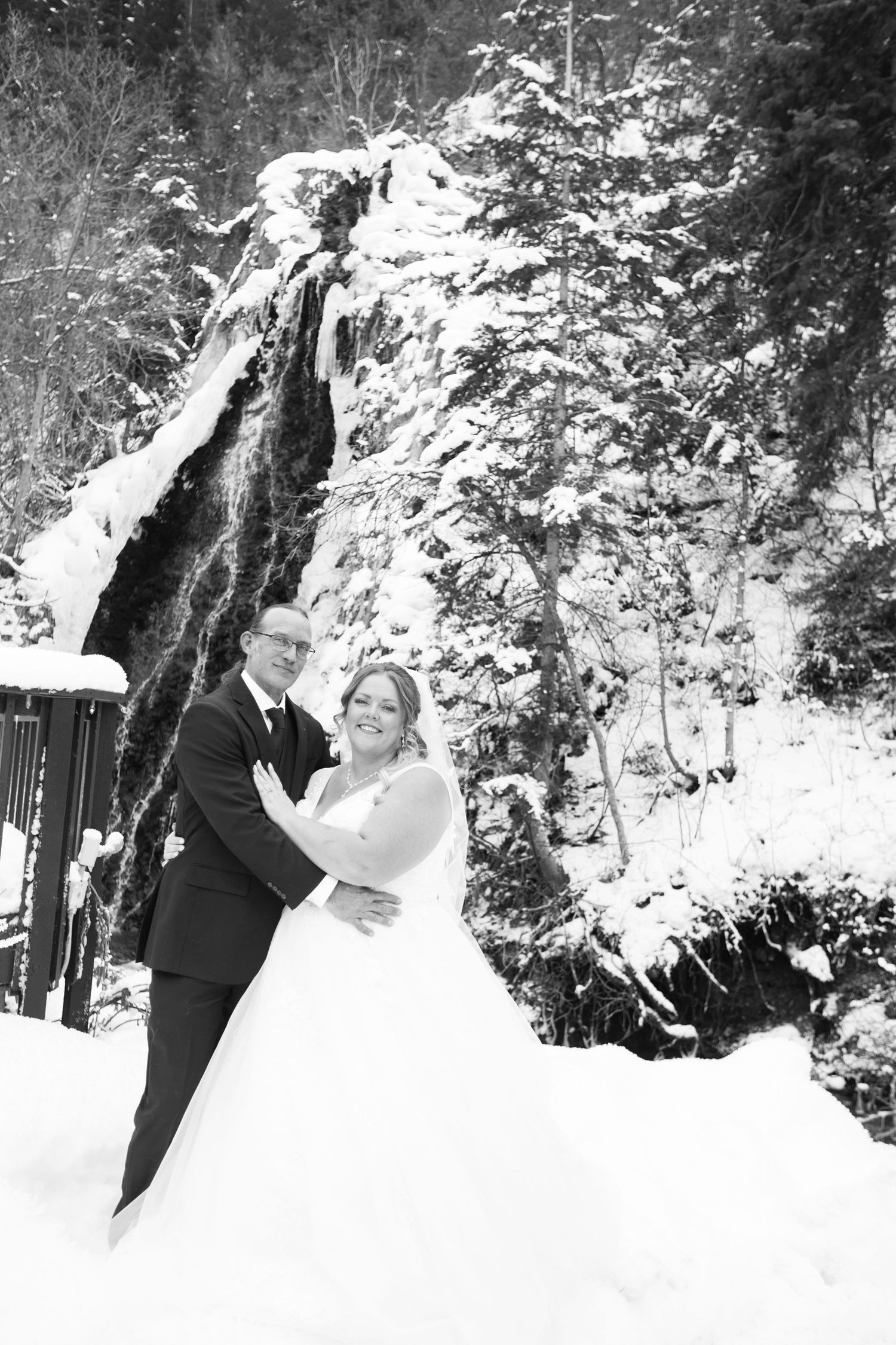 Wedding couple poses against snowy forest backdrop in black and white.