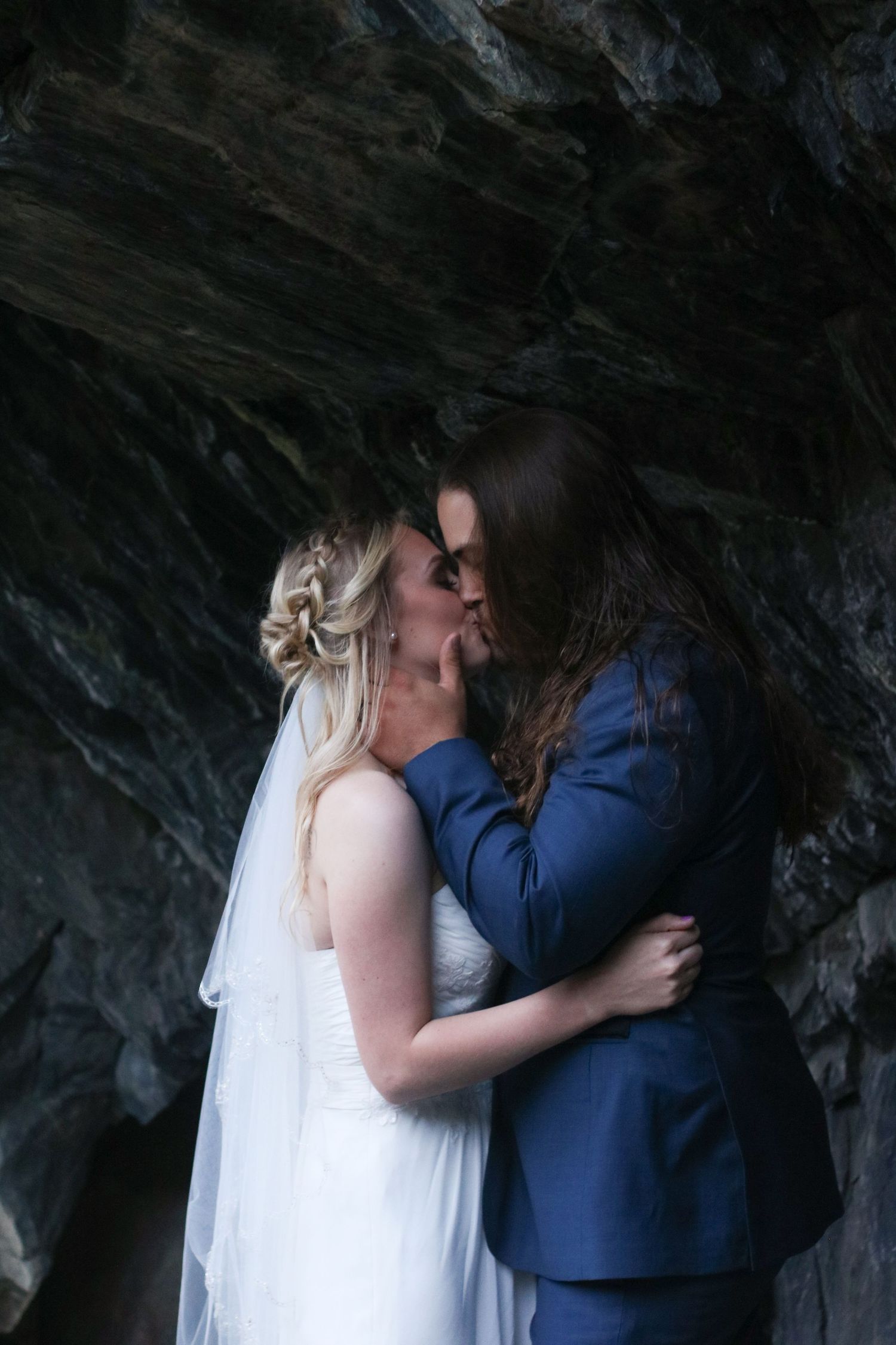 Dramatic wedding photos captured in dark cave setting with couple in formal attire.