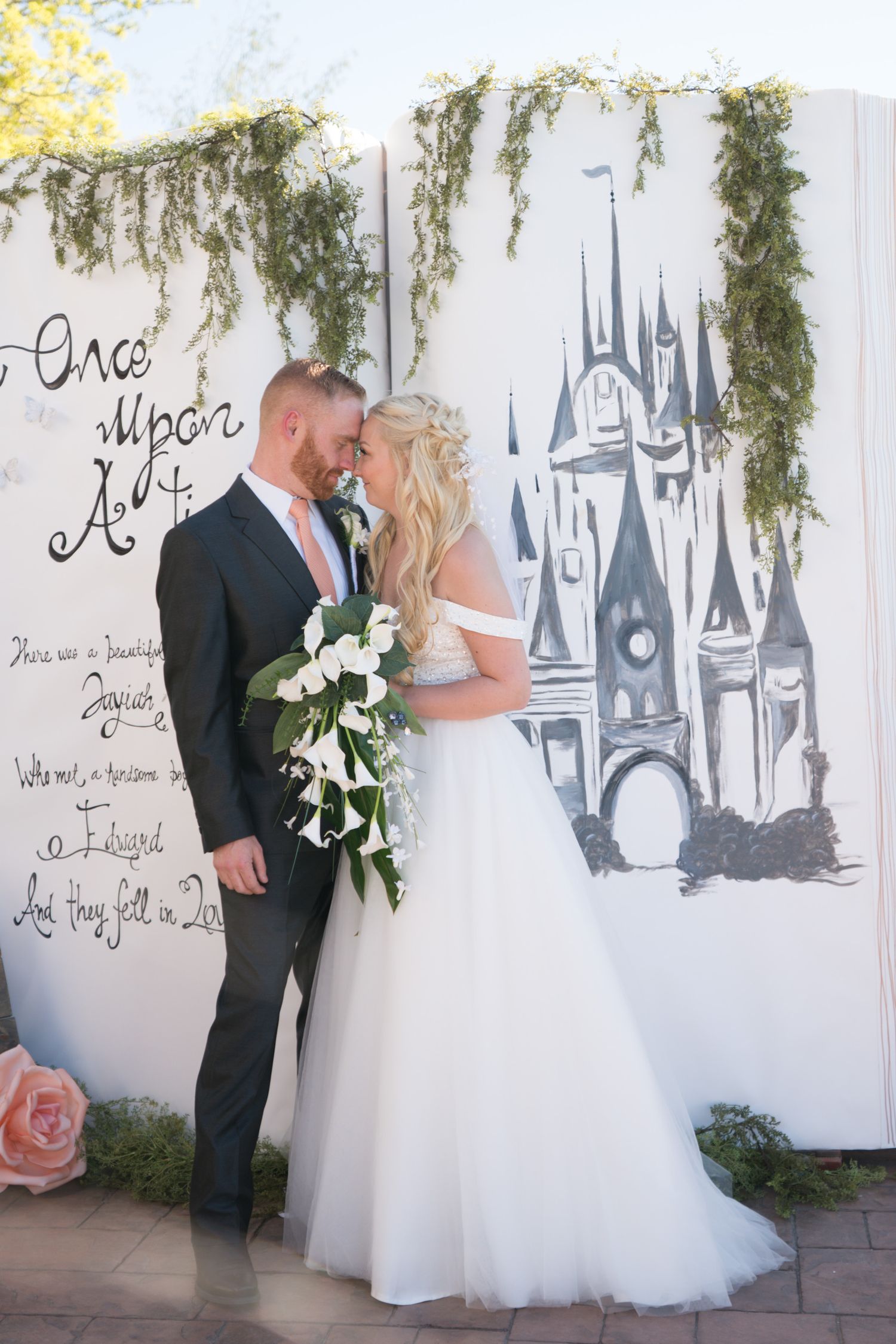 Wedding photos taken against a wall decorated with castle artwork and hanging vines.