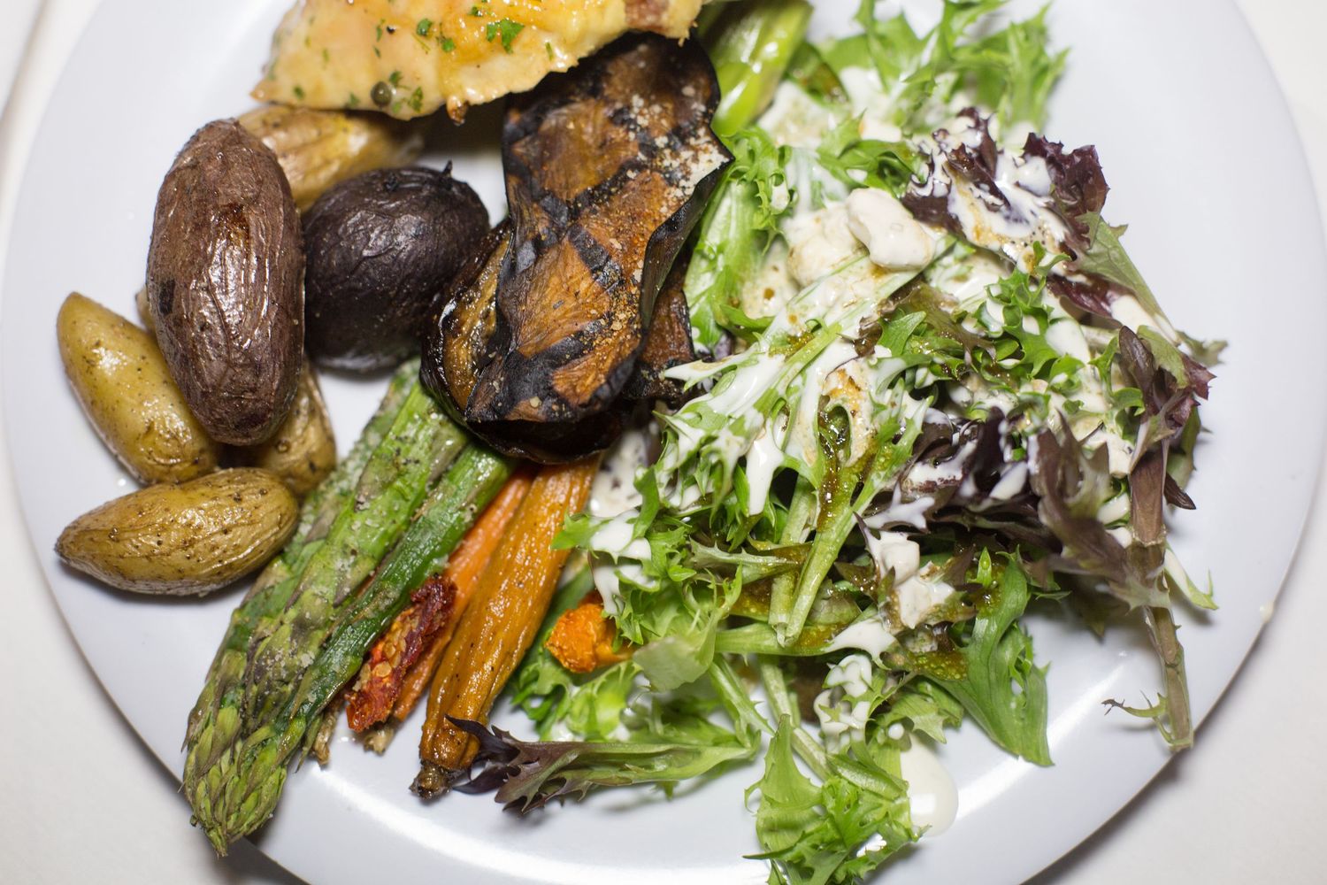 Roasted vegetables plate with asparagus, carrots, eggplant, potatoes, and fresh mixed greens salad on white plate.