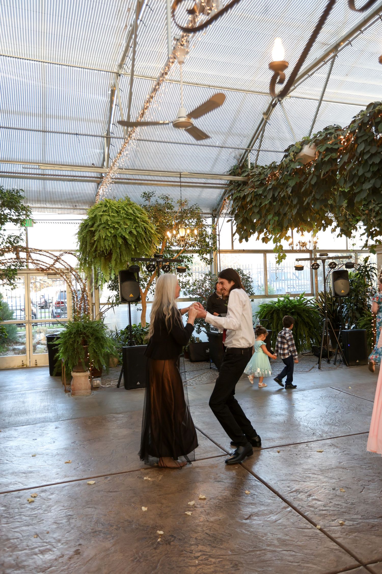 Couples dancing together on a concrete floor in a greenhouse wedding venue.