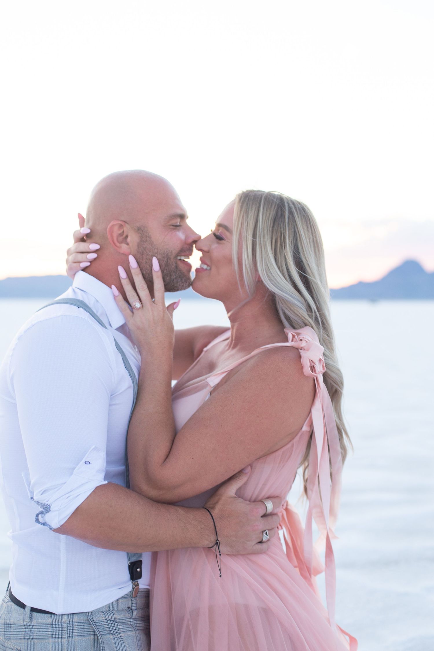 Couple shares romantic kiss during beach photoshoot at dusk.