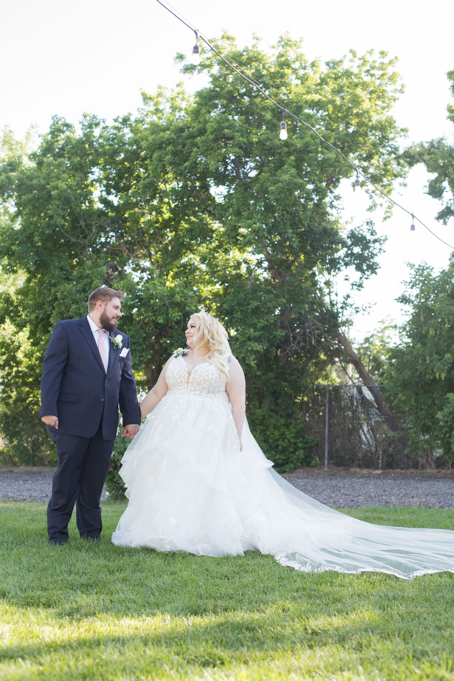 Couple poses together on grass in wedding attire during outdoor summer photo session.