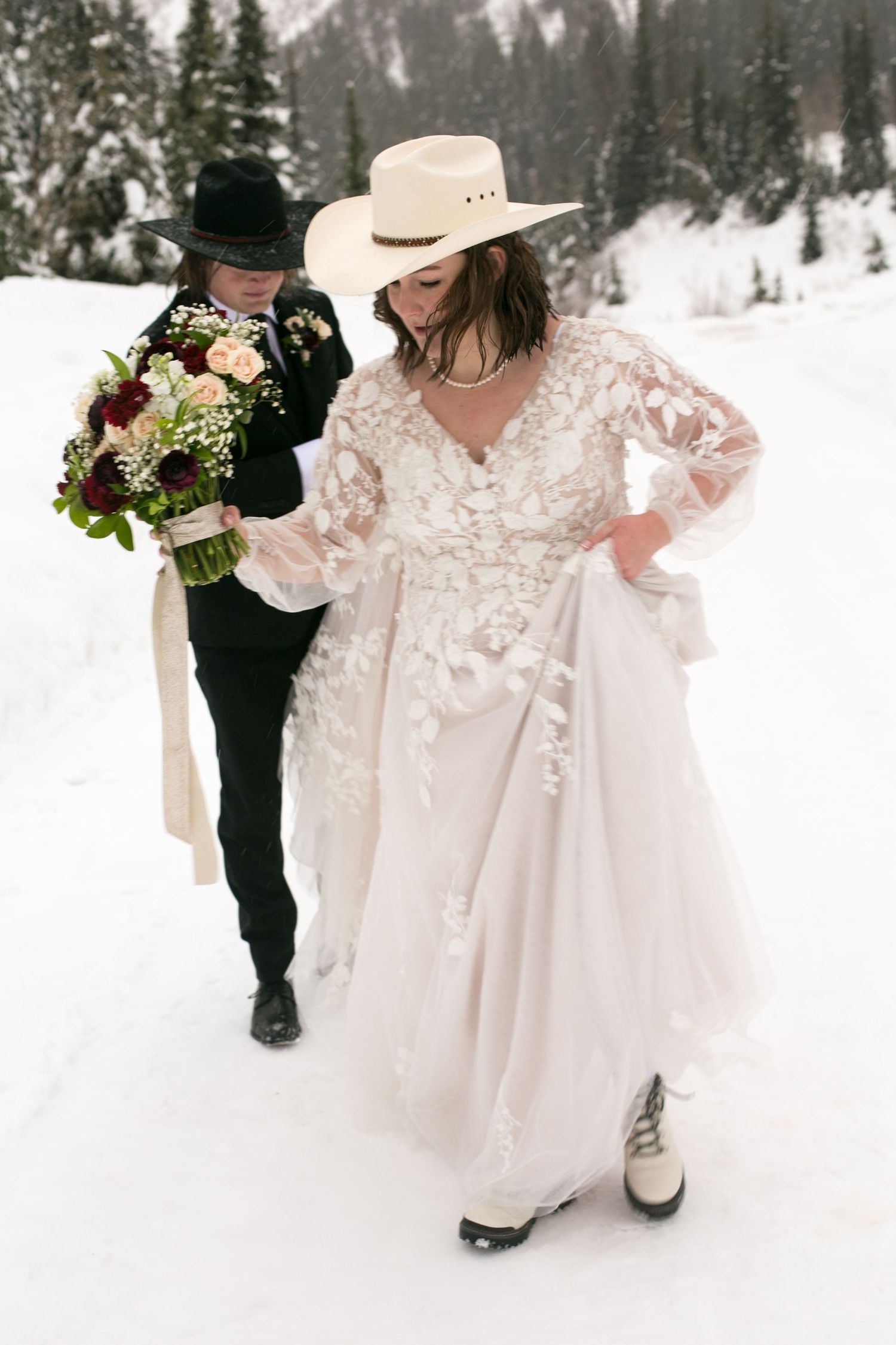 Wedding couple walking through snowy mountain landscape with evergreen trees.