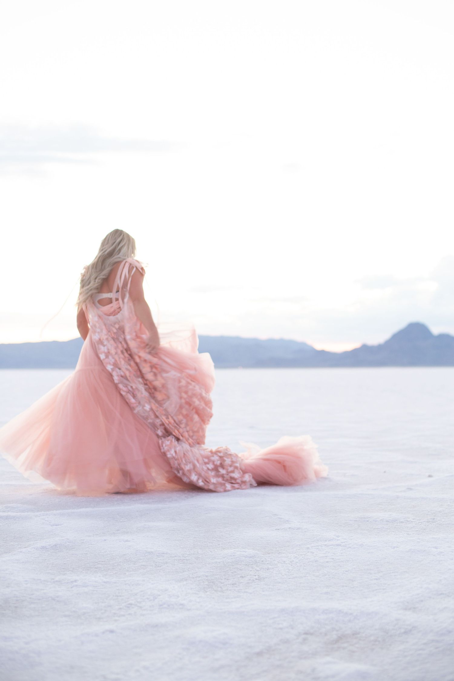 Pink lace gown sweeps across white sand creating romantic desert photography.
