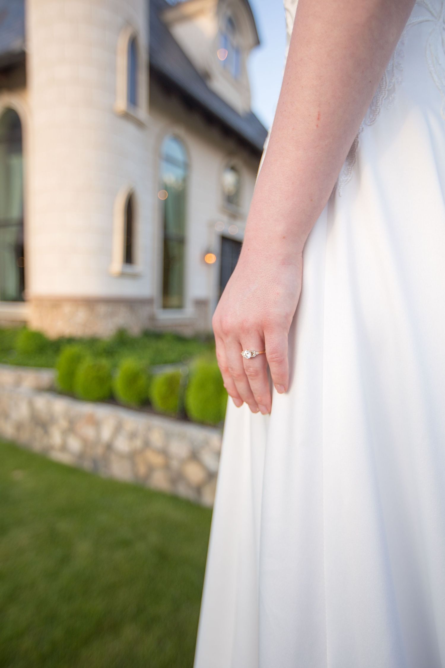 Close-up details of white wedding dress and ring against castle backdrop.