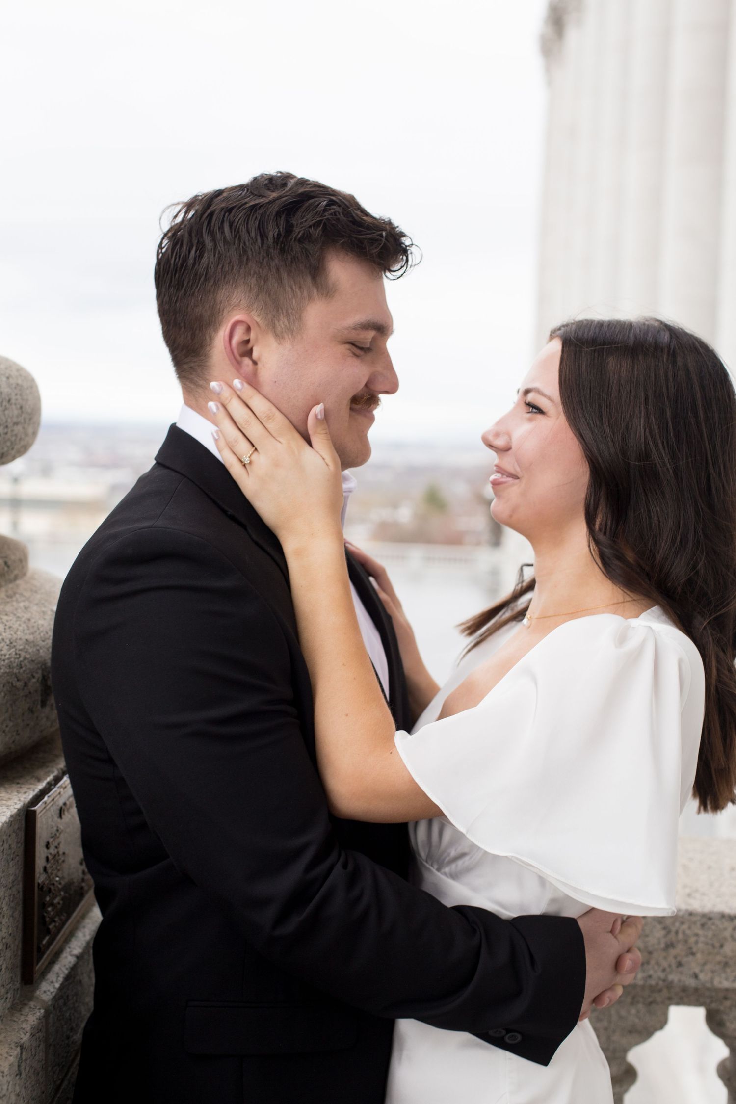 An intimate embrace between newlyweds on an ornate balcony with city views in the background.
