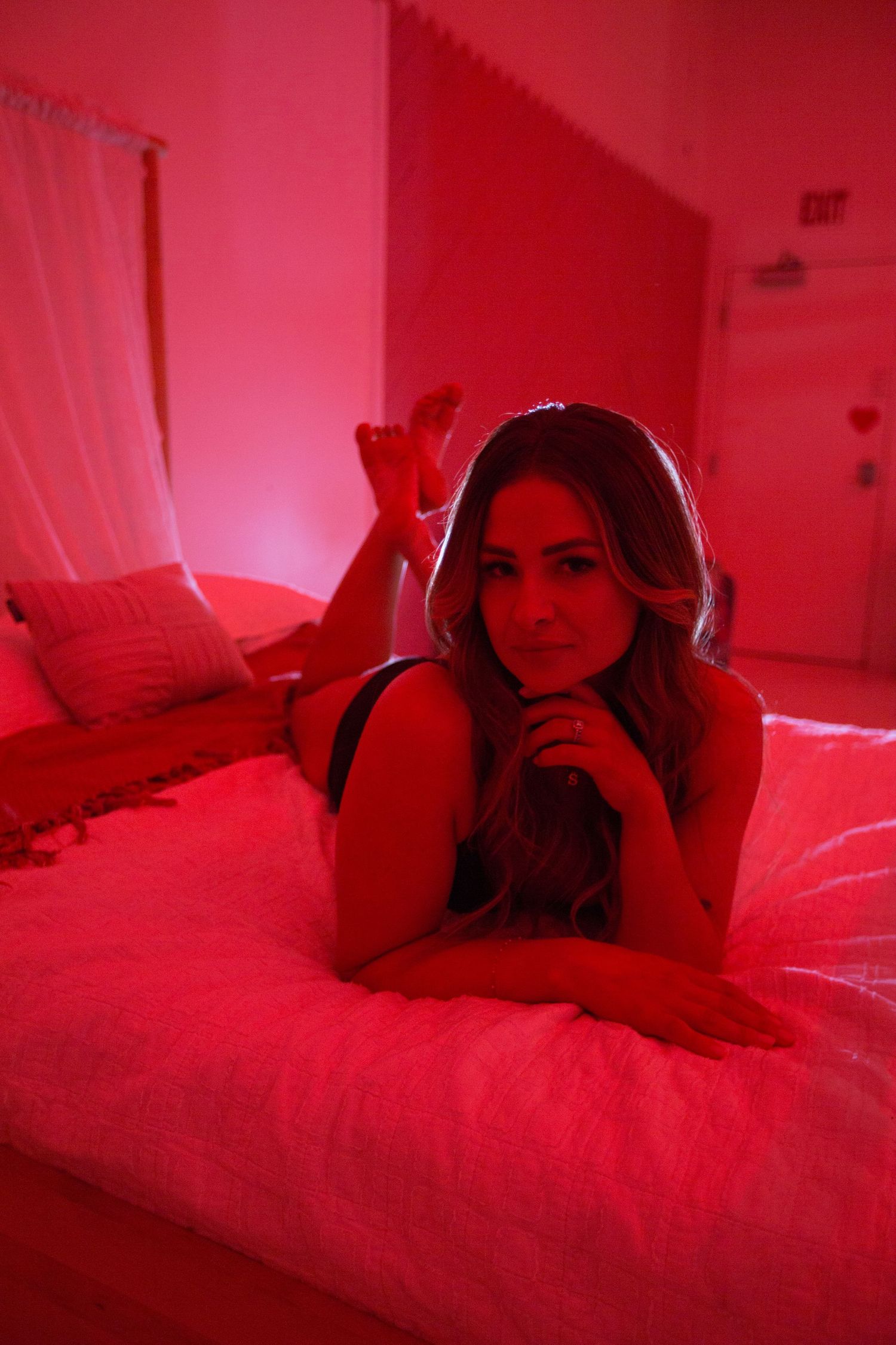 Person lying on bed bathed in red light creating moody atmosphere.