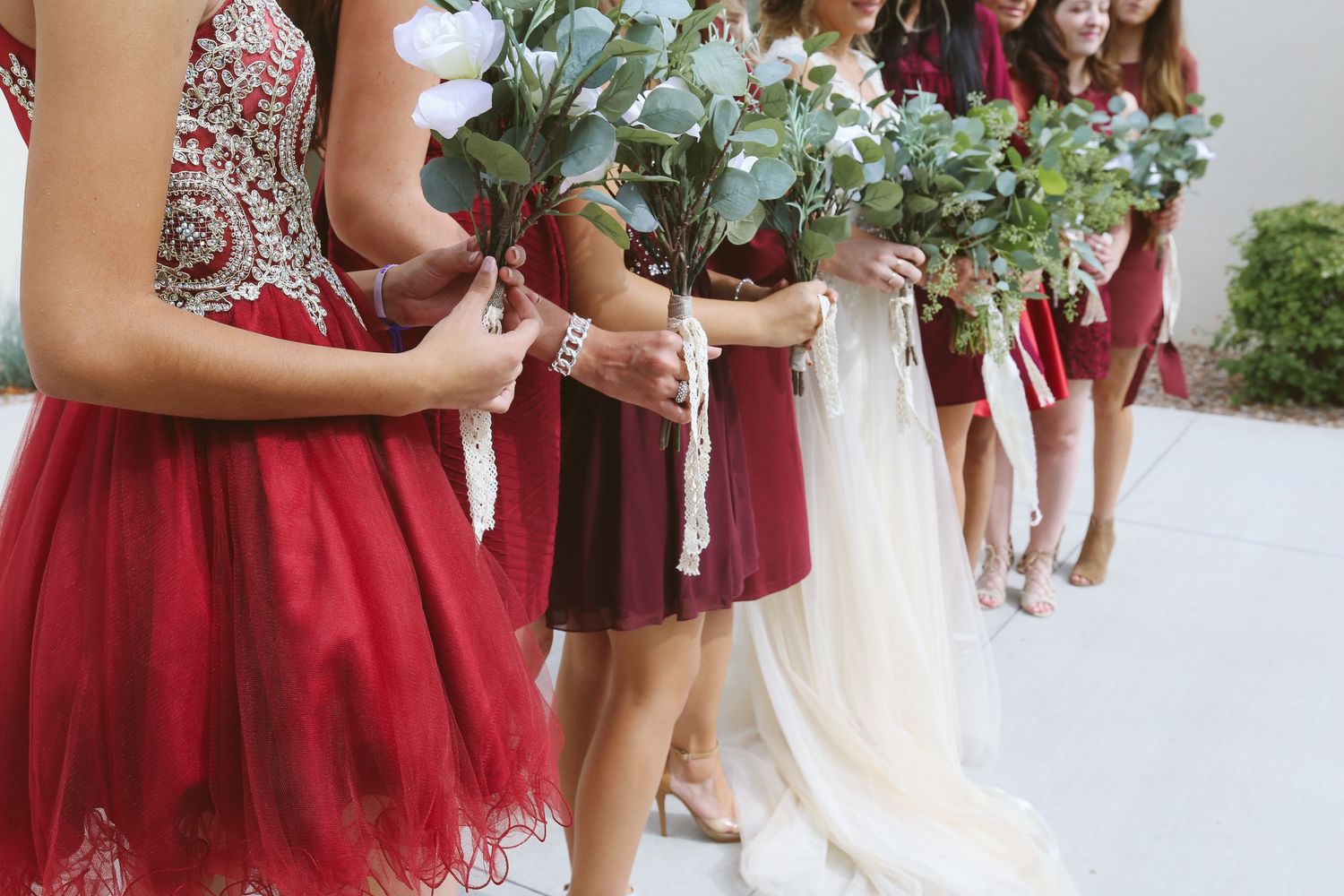 Bridesmaids in burgundy dresses hold bouquets during an outdoor wedding ceremony.