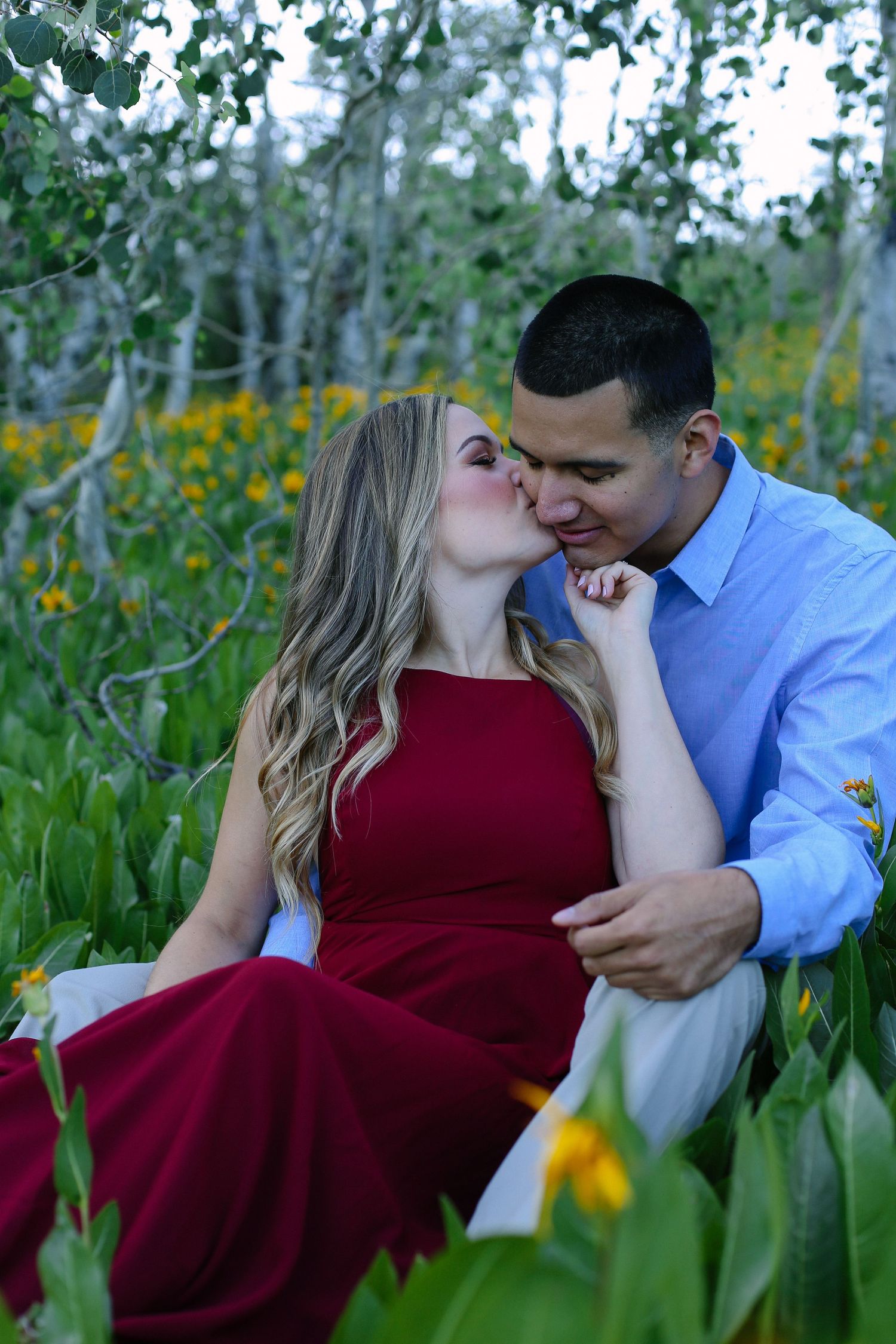Intimate moment between couple in burgundy dress and blue shirt among yellow wildflowers.