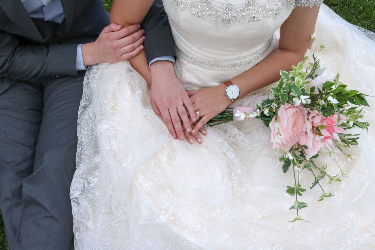 Close-up details of a white lace wedding dress and pink floral bouquet.