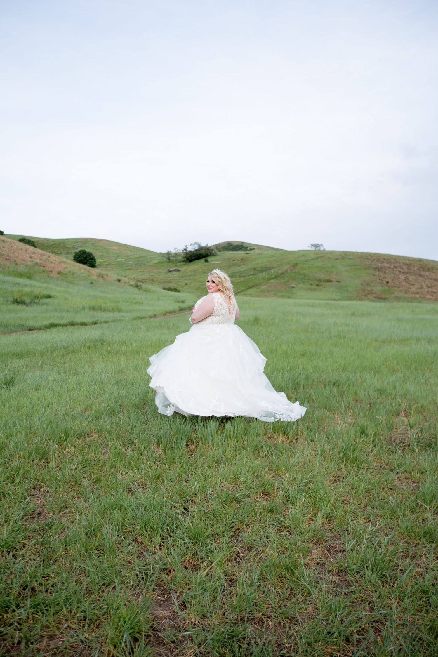 White wedding dress flowing across a green hillside meadow in a series of romantic bridal portraits.
