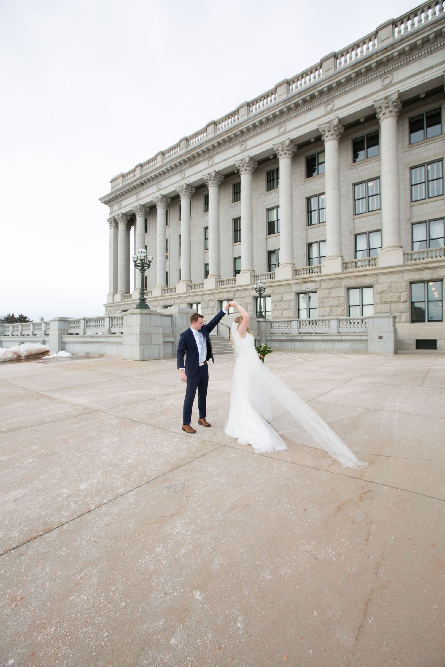 Wedding couple poses on grand stone steps of a historic building with elegant architecture.