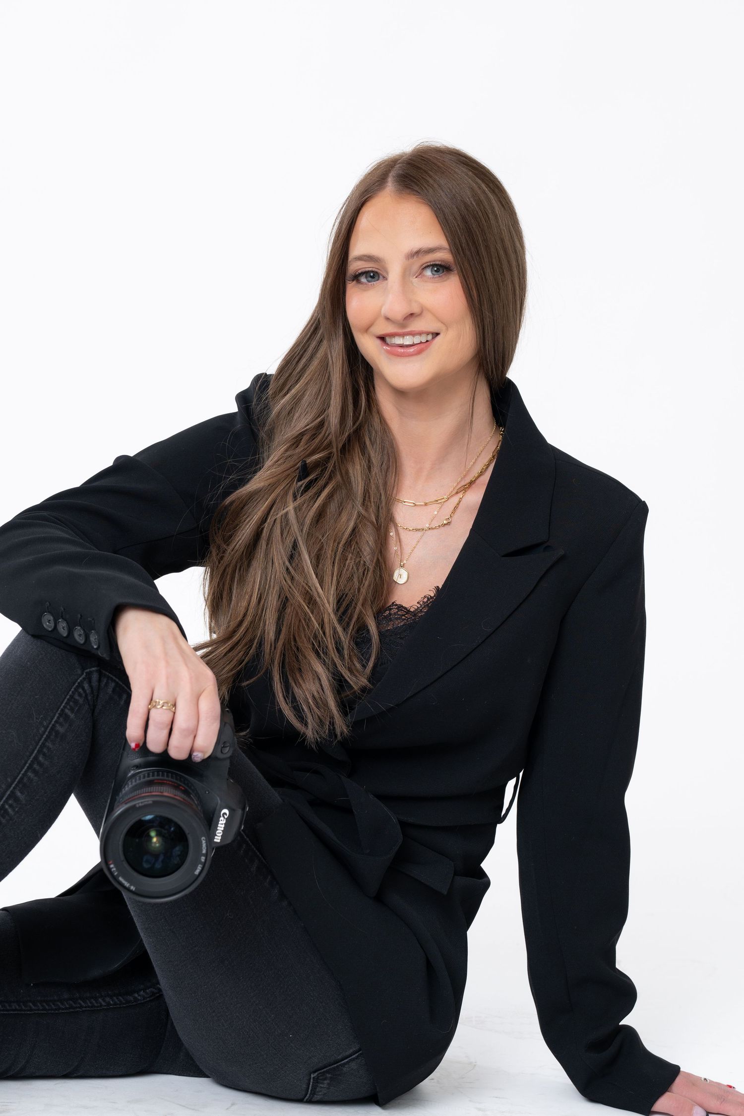 Professional photographer in black blazer posing with camera on white background.