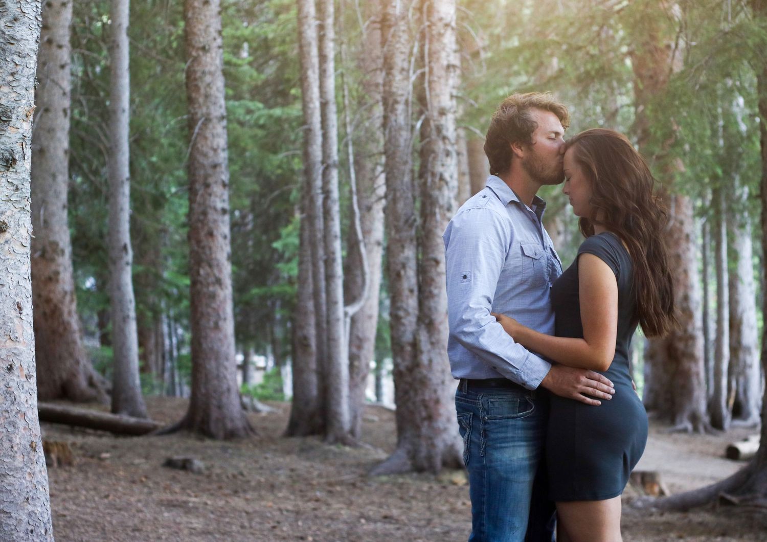 A romantic forest engagement photo with sunlight filtering through birch trees.