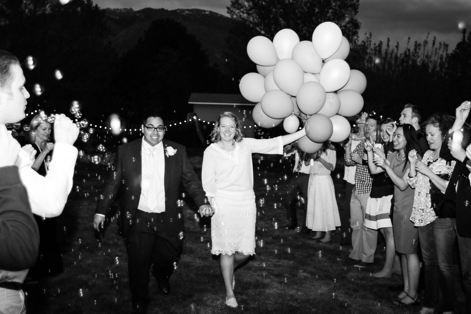 Black and white celebration scene with white balloons and festive crowd.