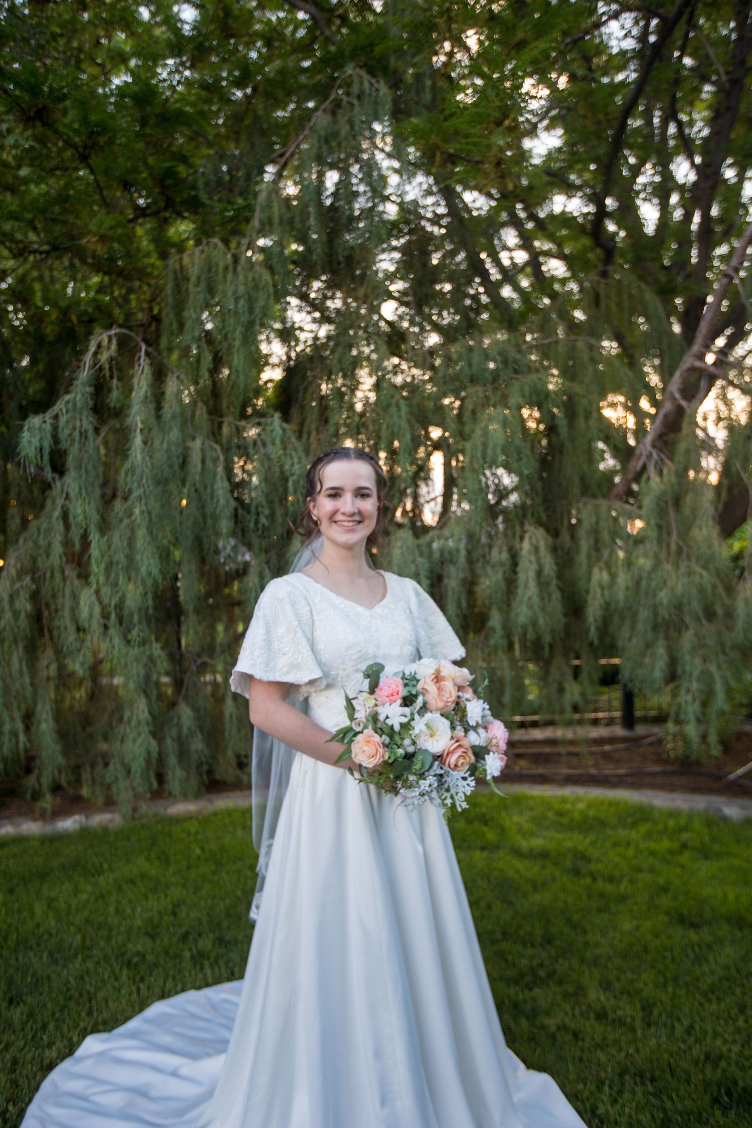 A white wedding gown with a bouquet of pink and white flowers in a garden setting.