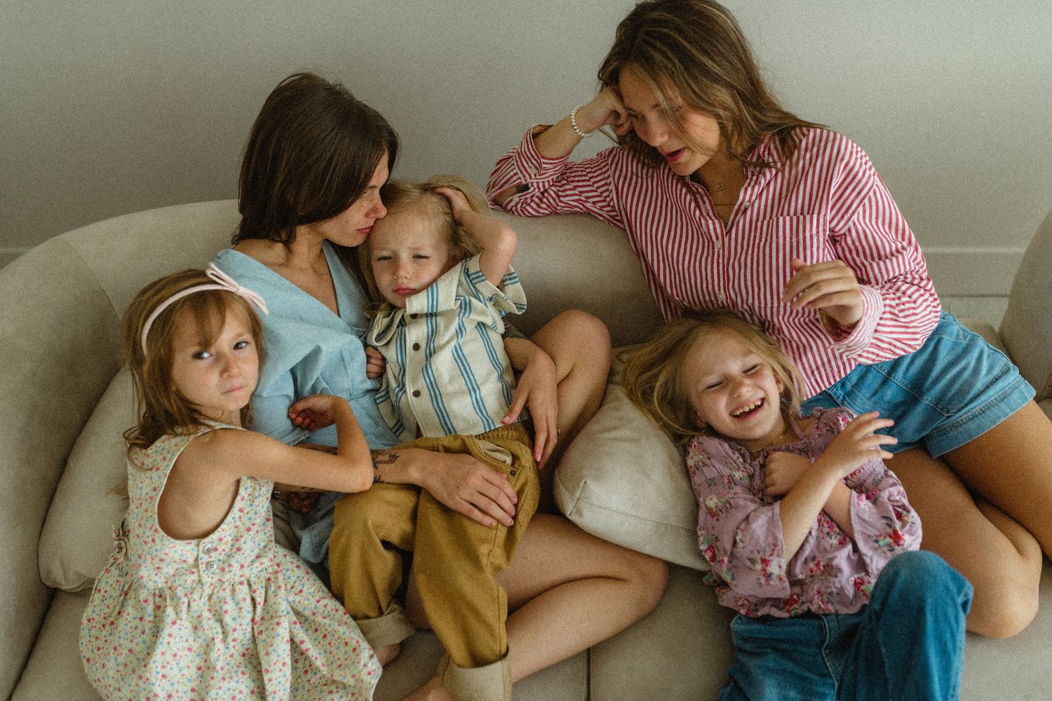 Two mothers sitting on a couch laughing with their three young children.